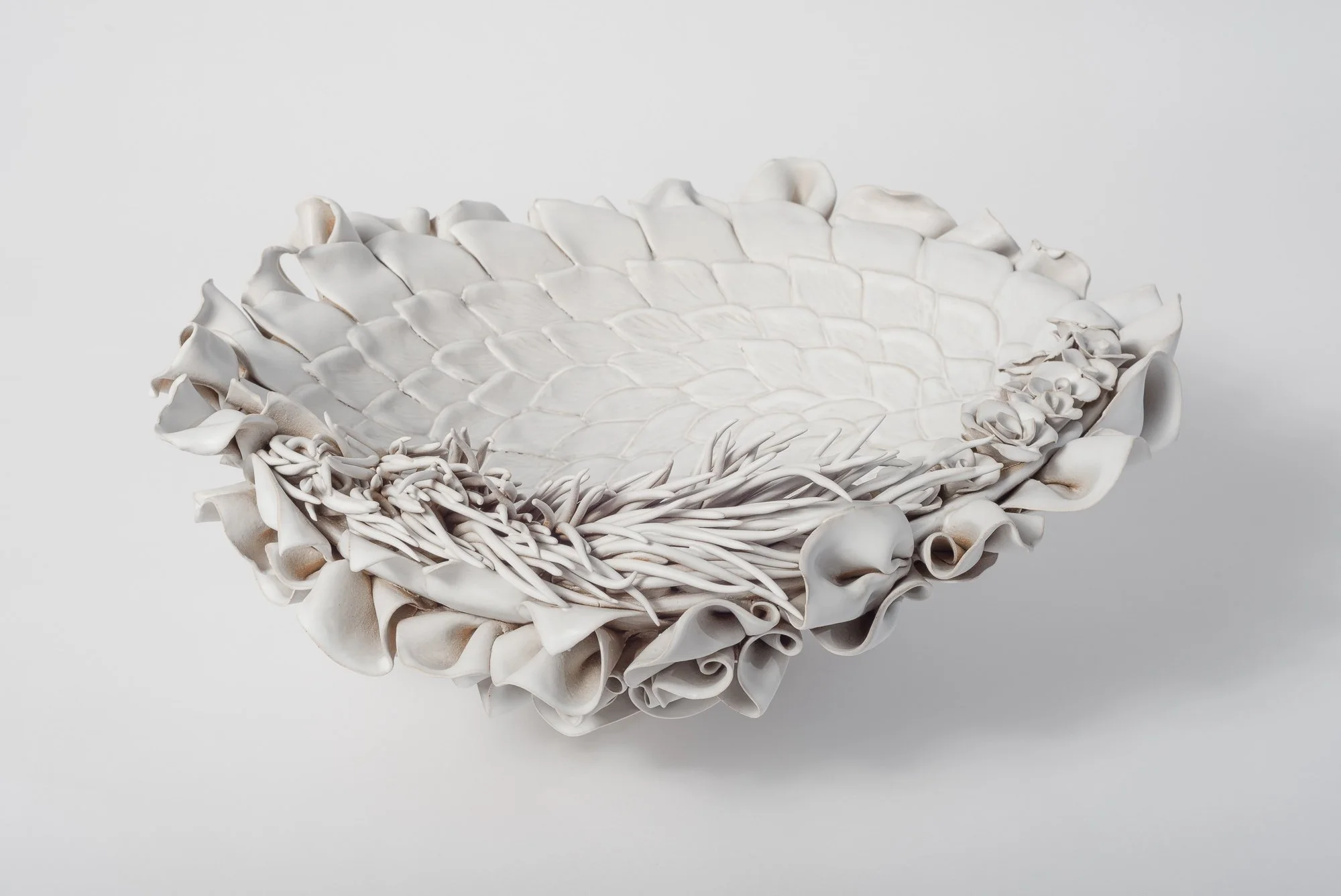 White ceramic bowl with intricate petal and floral design on a plain white background.