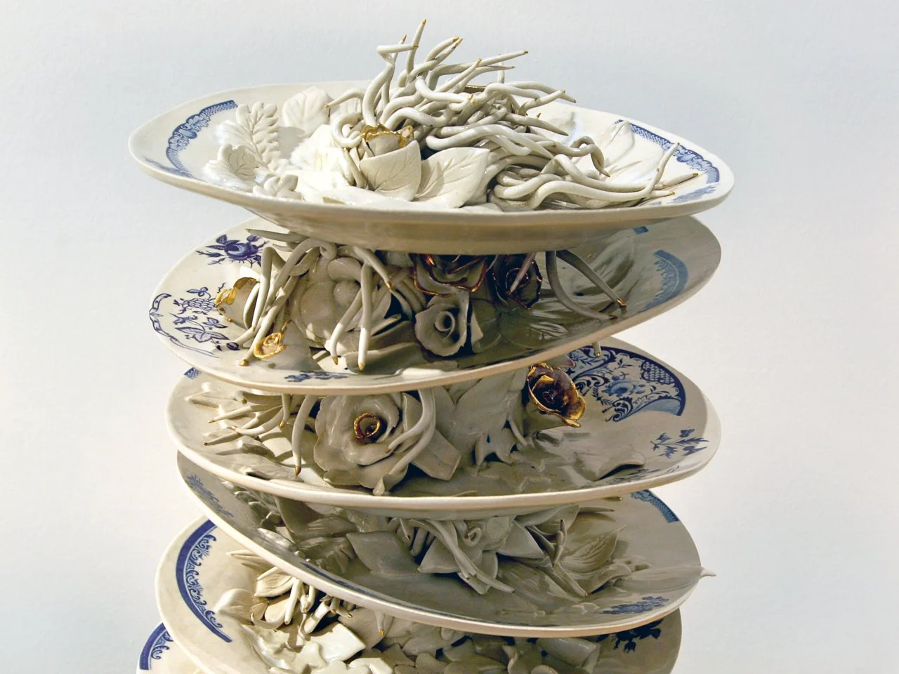 Stacked ceramic plates with intricate blue patterns, filled with white ceramic sculptures resembling abstract organic forms.