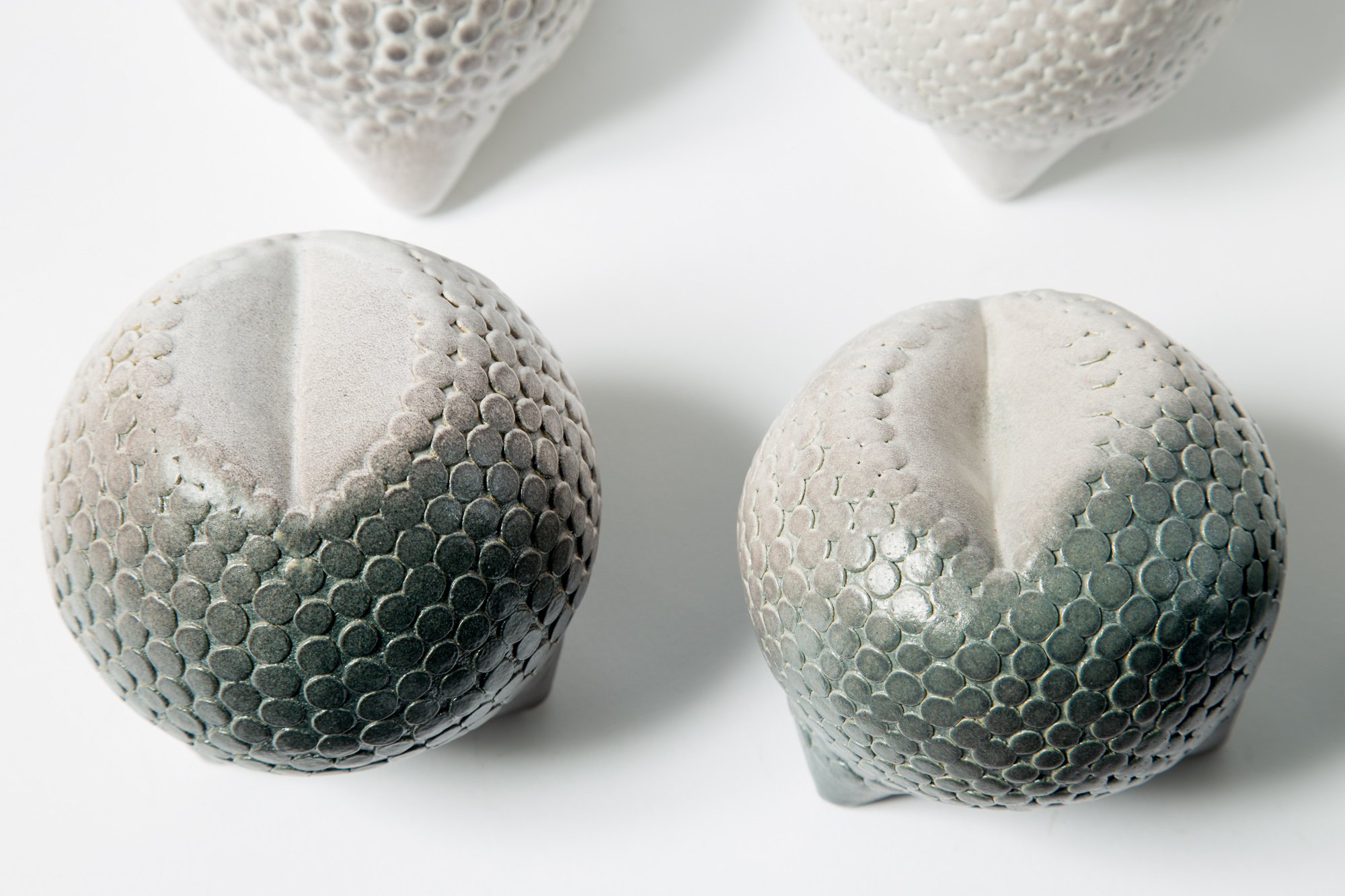 Close-up of four textured gray ceramic vases with circular patterns, positioned on a white surface.