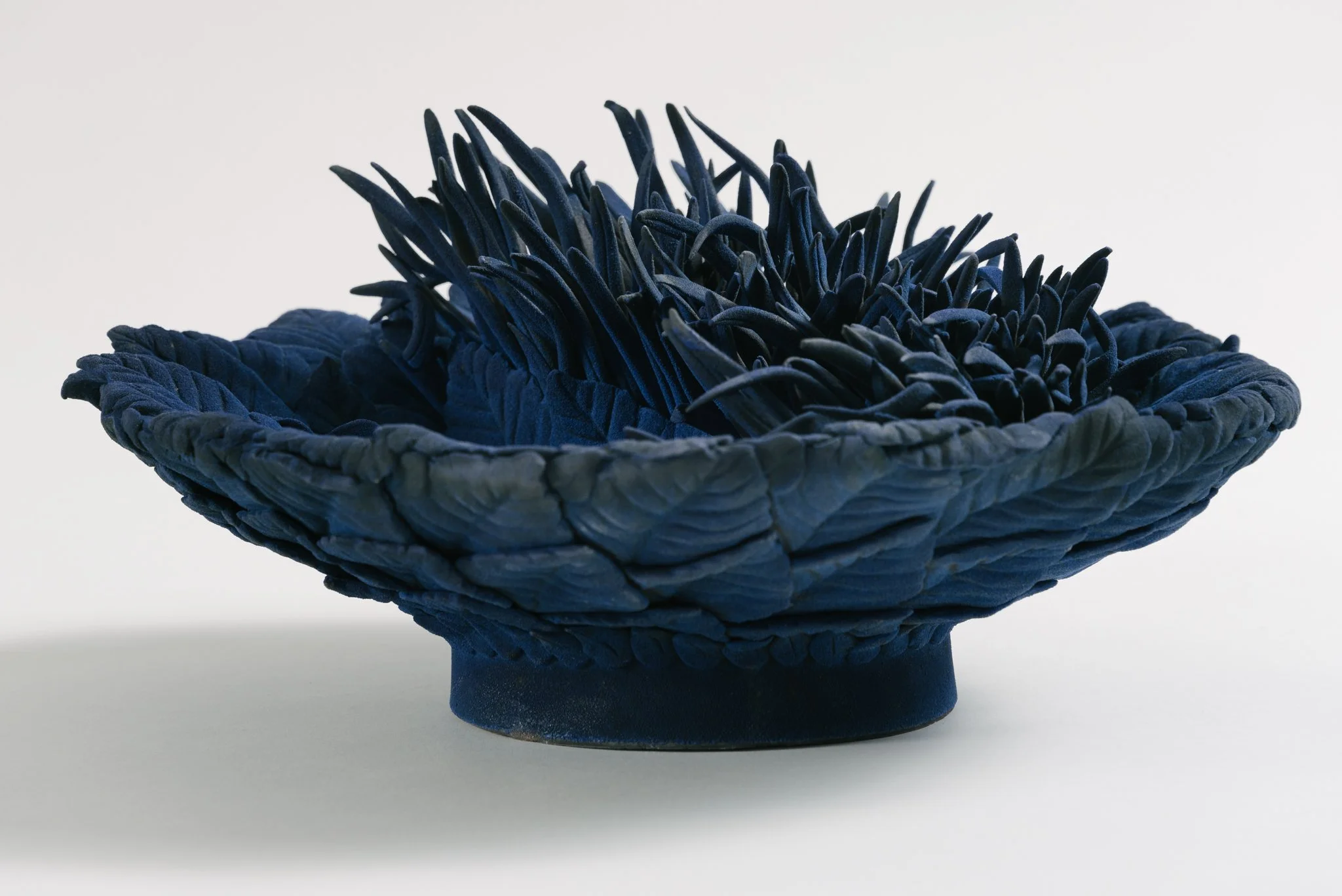 A dark blue woven basket with a textured surface and a wide, flat side, placed against a plain white background.