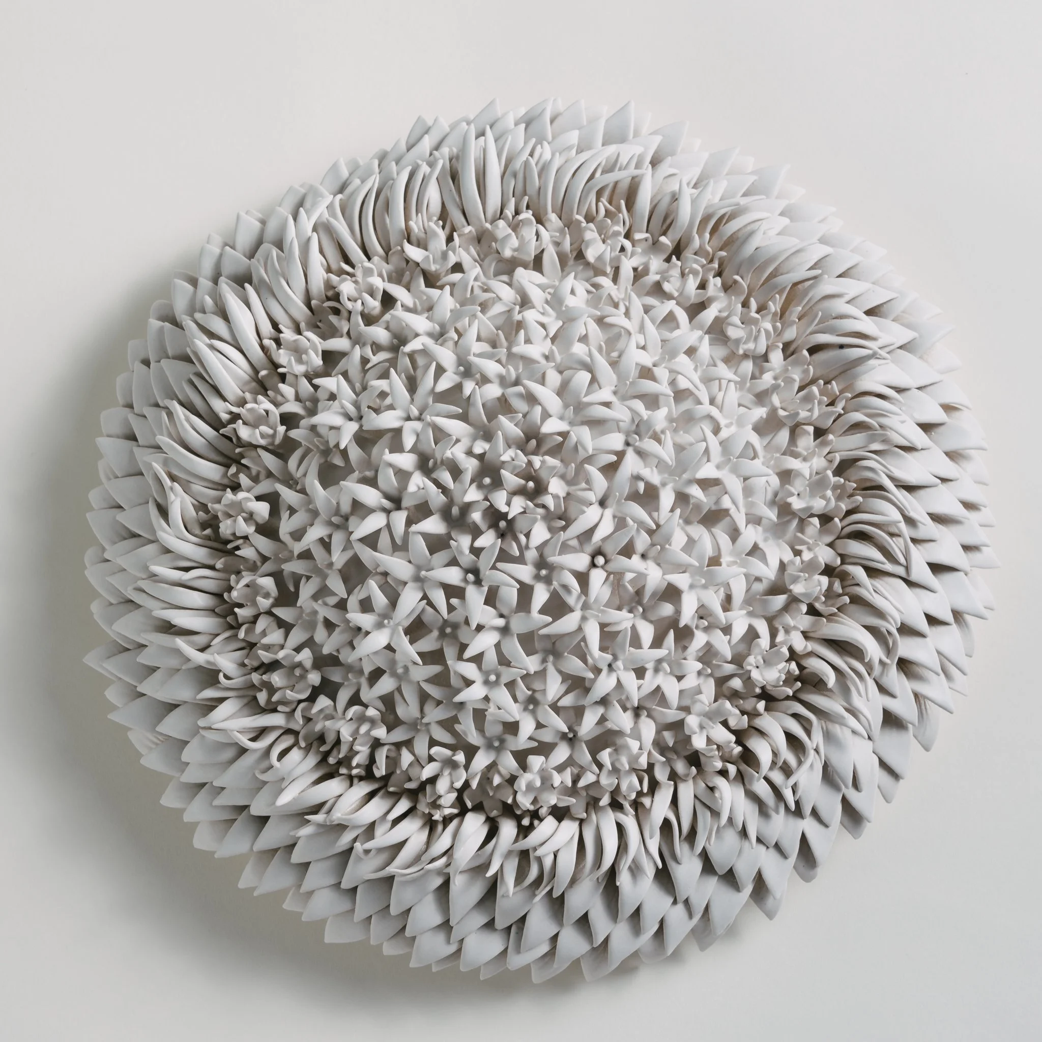 A close-up image of a white, textured, spherical sculpture made of numerous small, pointed, leaf-like shapes arranged densely together.
