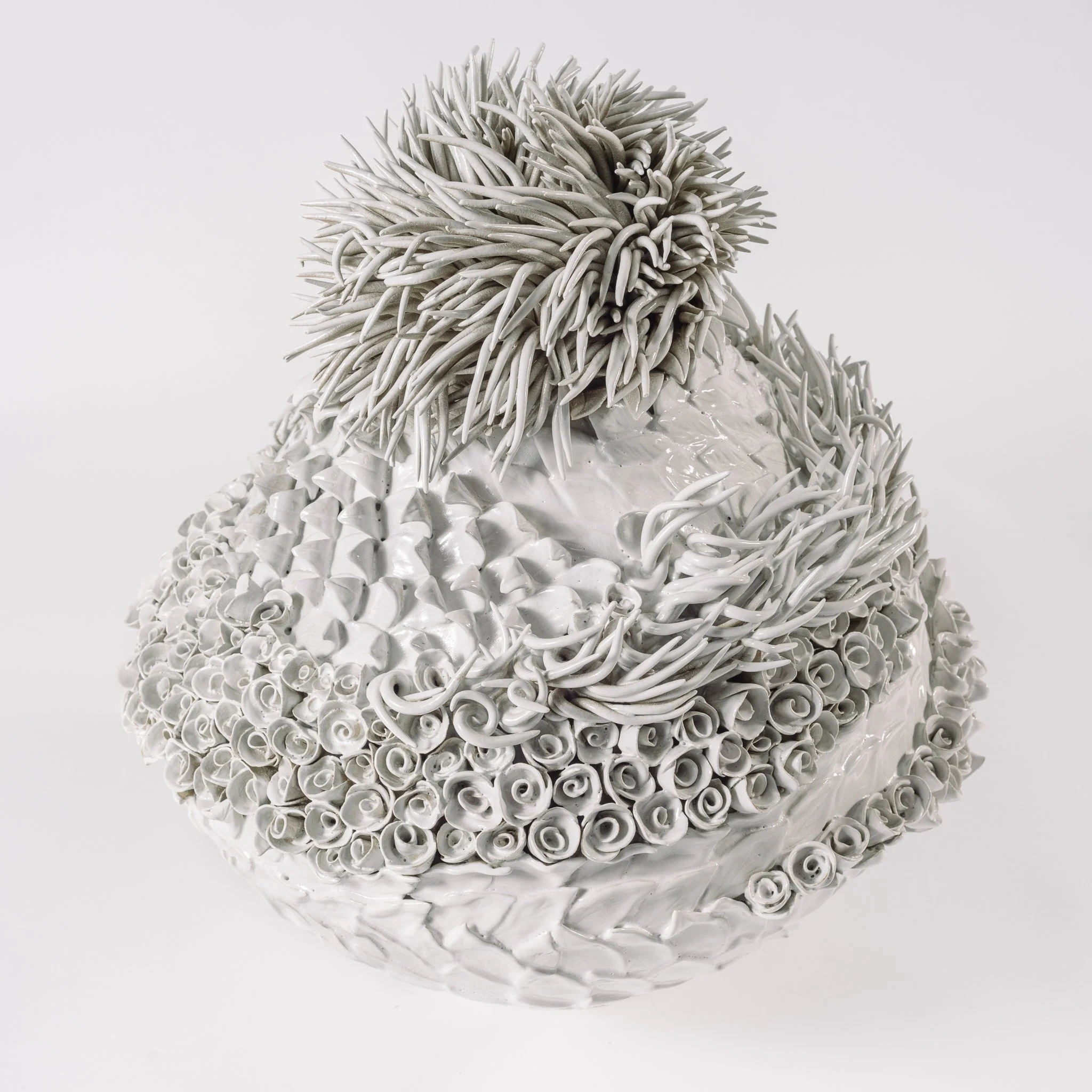 A white sculpture resembling a mountain, made of twisted, tubular forms with spiky, elongated elements on top, set against a plain light background.