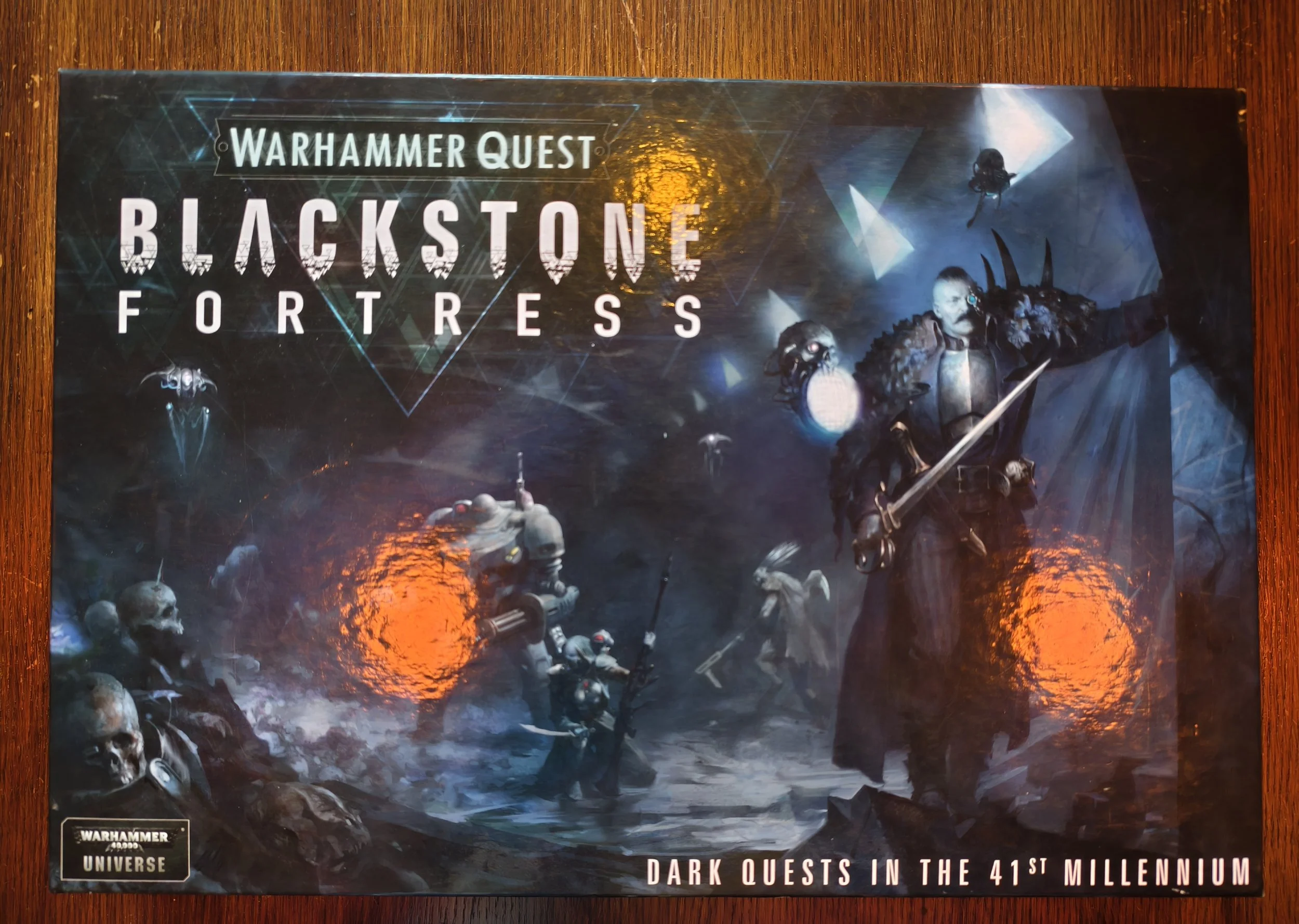 A promotional poster for Warhammer Quest: Blackstone Fortress featuring sci-fi artwork with characters, skulls, and futuristic elements, and the tagline "Dark Quests in the 41st Millennium."