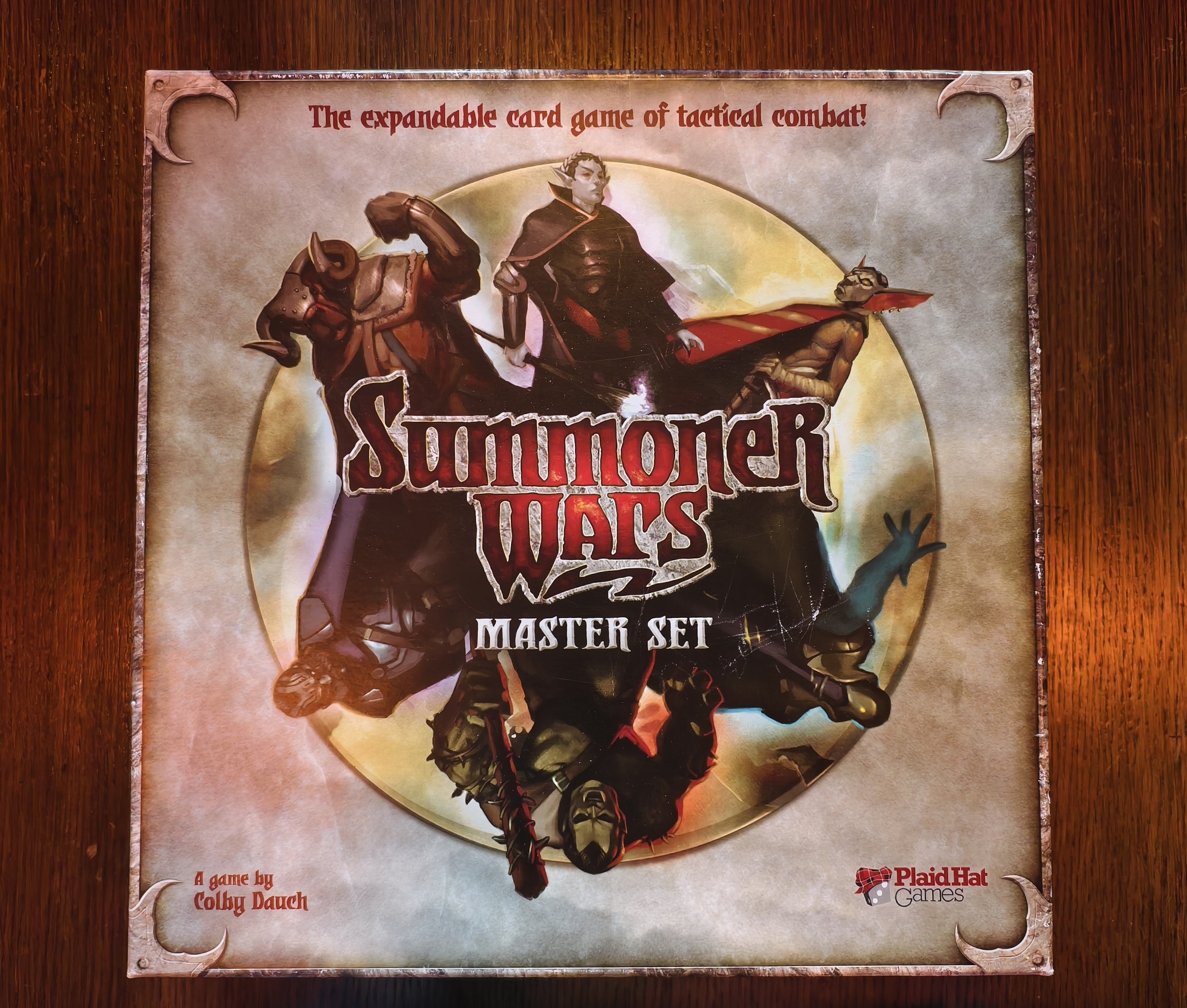 Game box titled 'Summoner Wars Master Set' featuring fantasy characters including a human, a creature with horns, and a goblin, with text 'The expandable card game of tactical combat!' at the top.