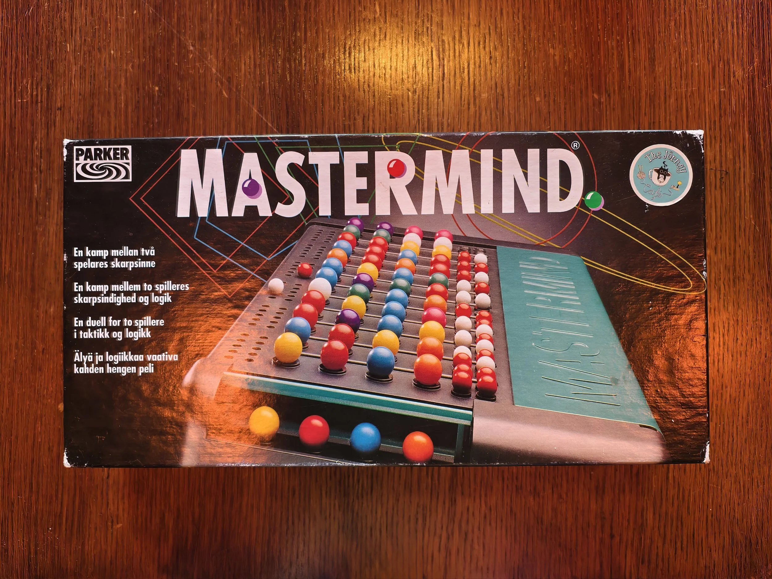 The image shows a boxed tabletop game called Mastermind, which is a code-breaking game for two players, featuring colorful balls and a game board.
