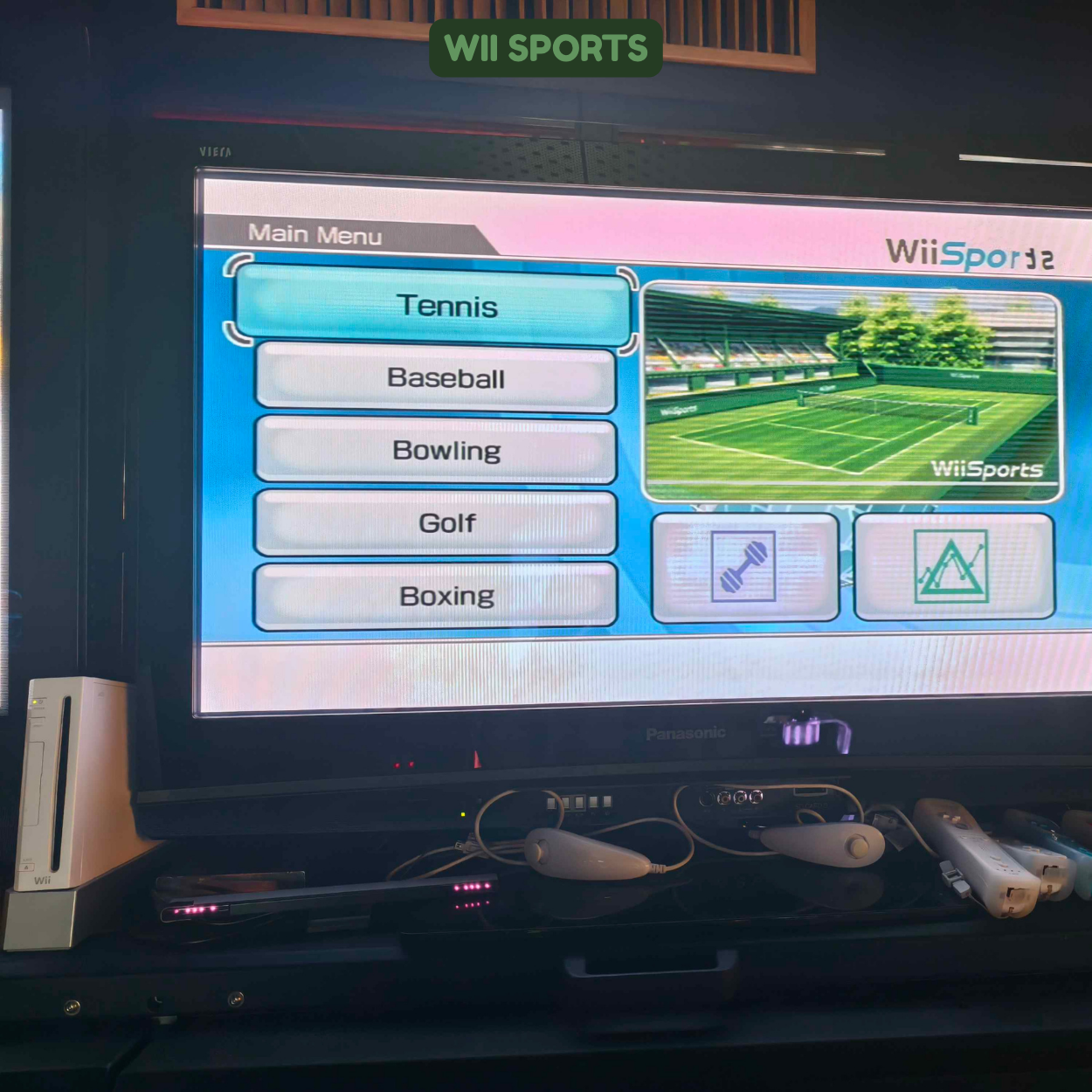 TV screen displaying a Wii Sports menu with options for tennis, baseball, bowling, golf, and boxing. The selected game is tennis, showing a tennis court image. Play controllers and other electronics are visible in front of the TV.