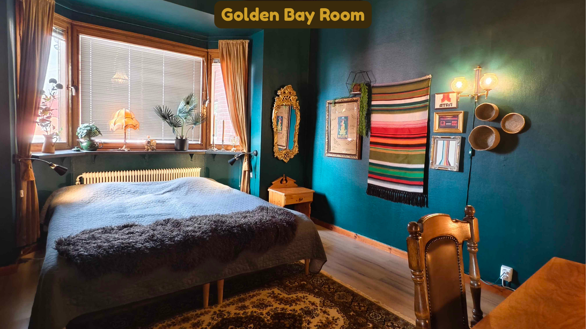A cozy bedroom with a blue wall, a window with blinds and golden curtains, a bed with a gray cover and a furry throw, and various decorative elements including potted plants, vintage frames, and wall art.