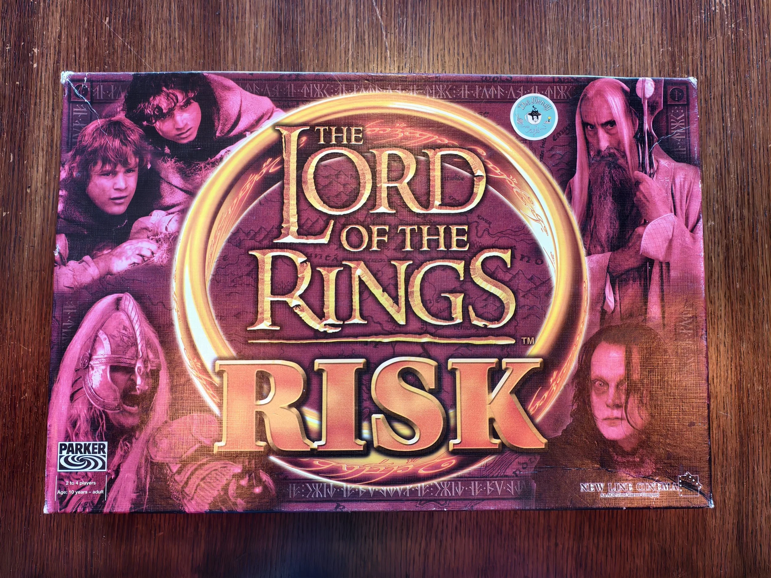 Close-up of a board game box for 'The Lord of the Rings' with illustrations of characters and symbols from the franchise, placed on a wooden surface.