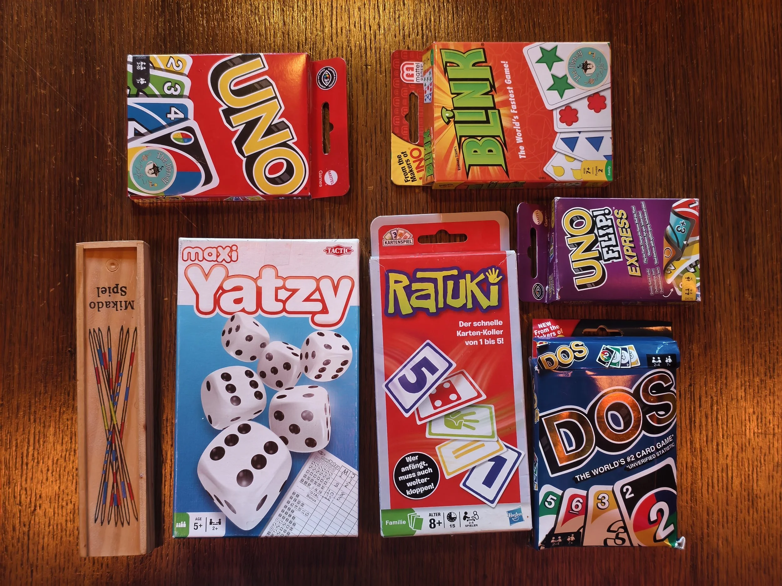 Collection of board and card games laid out on a wooden surface, including UNO, BIBER, and Yatzy.