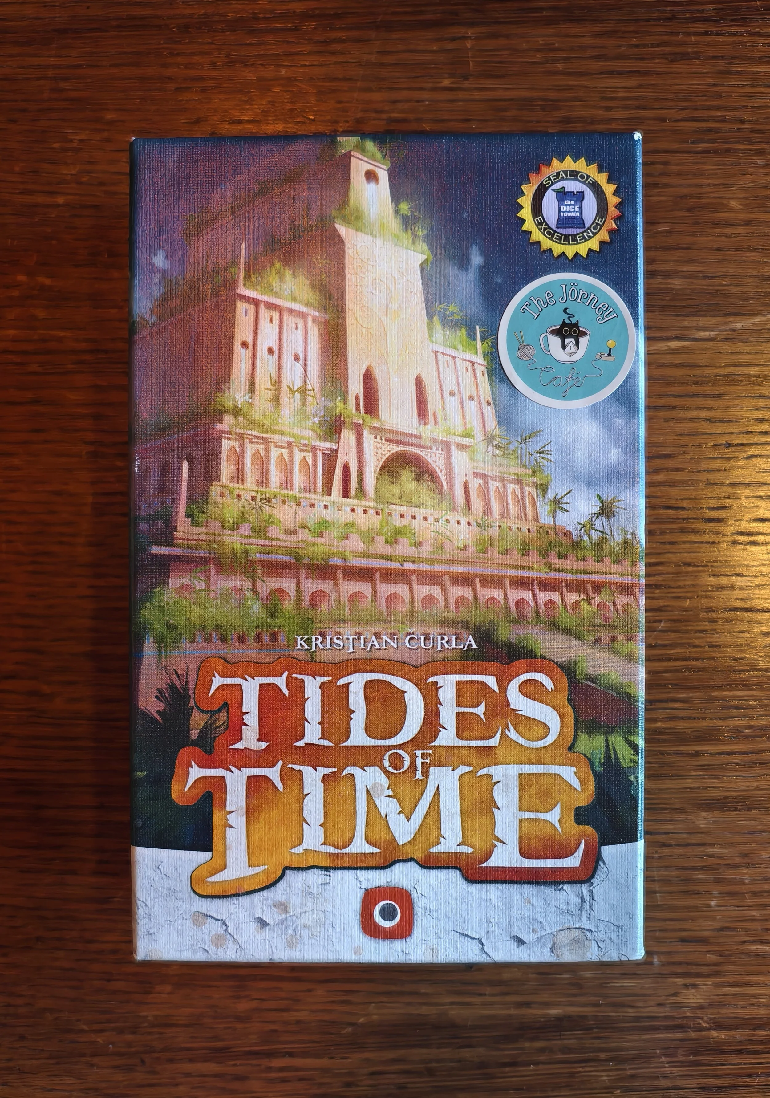 The cover of the book "Tides of Time" by Kristian Curla, featuring an illustrated castle on a hill with surrounding greenery and a cloudy sky, on a wooden surface.