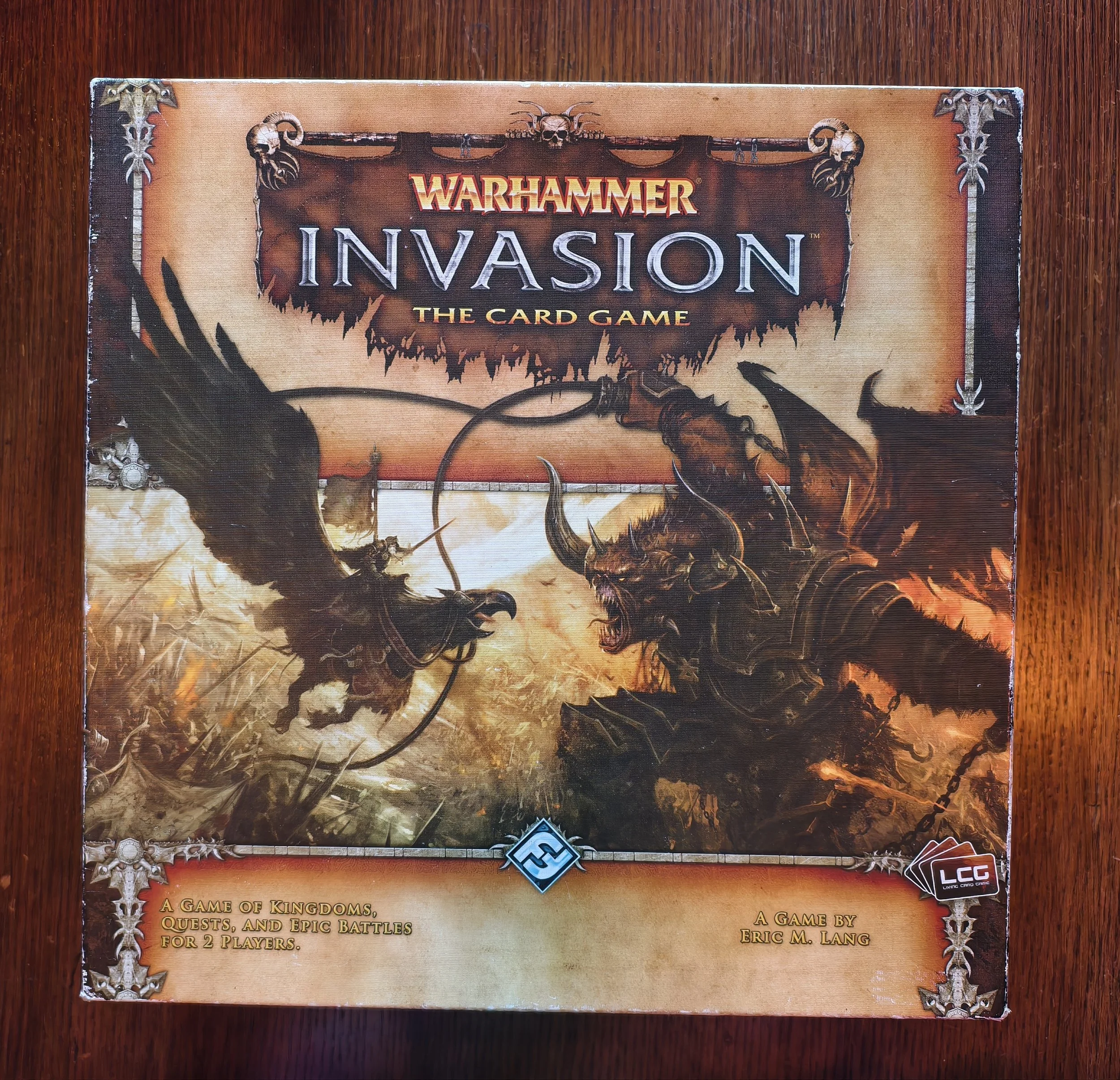 Box art for the game Warhammer Invasion: The Card Game, featuring a dark fantasy illustration of a dragon and a skull-themed border.