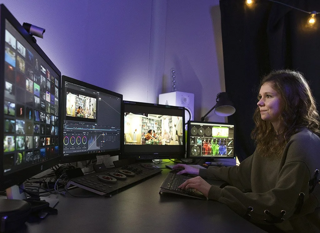 A workspace at The Jörniverse. An indie dev is using a multi-monitor setup in a dark room with ambient string lights.