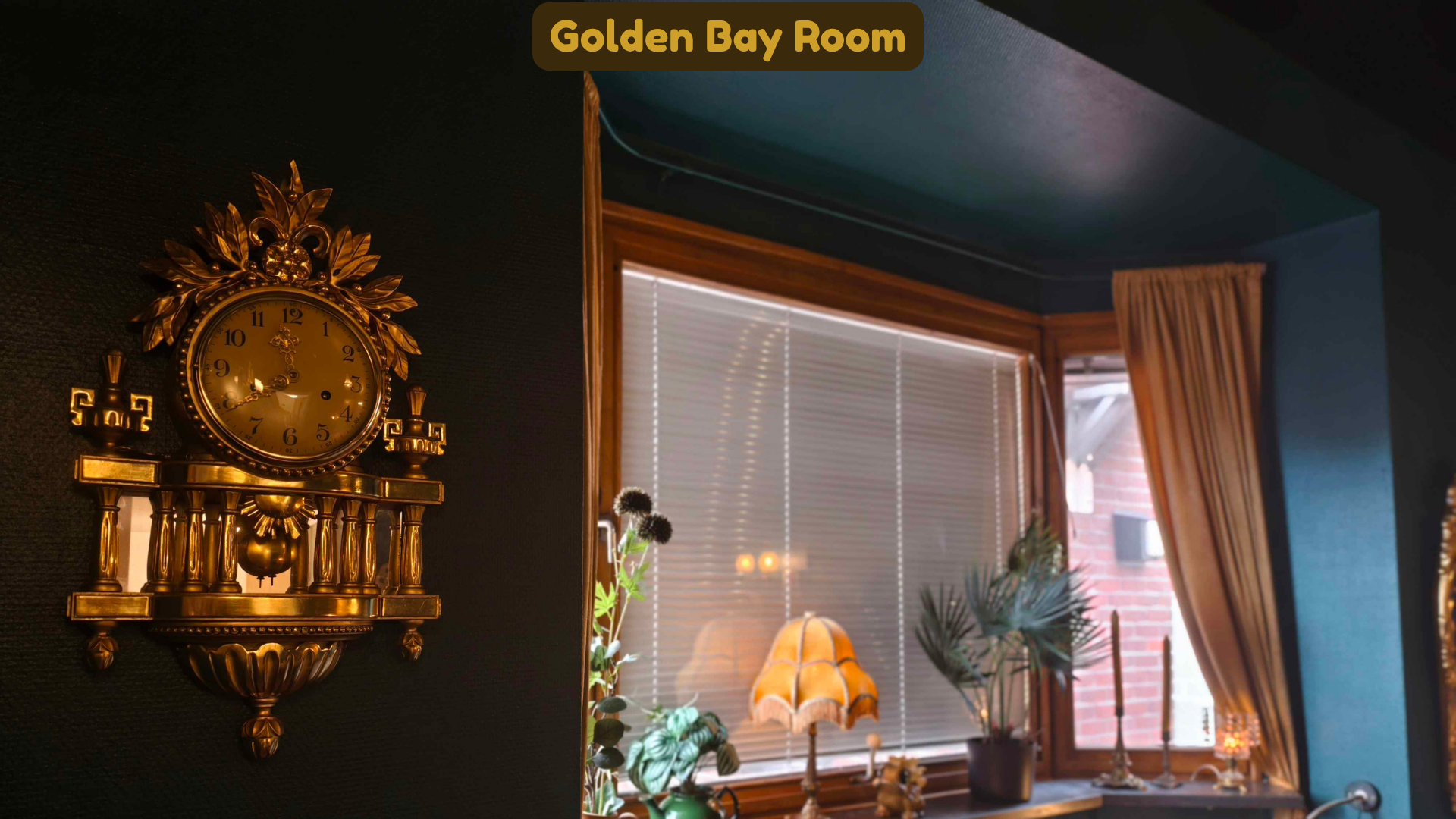 Vintage gold wall clock with ornate design hanging on a dark wall in a room with large windows, beige curtains, and indoor plants.