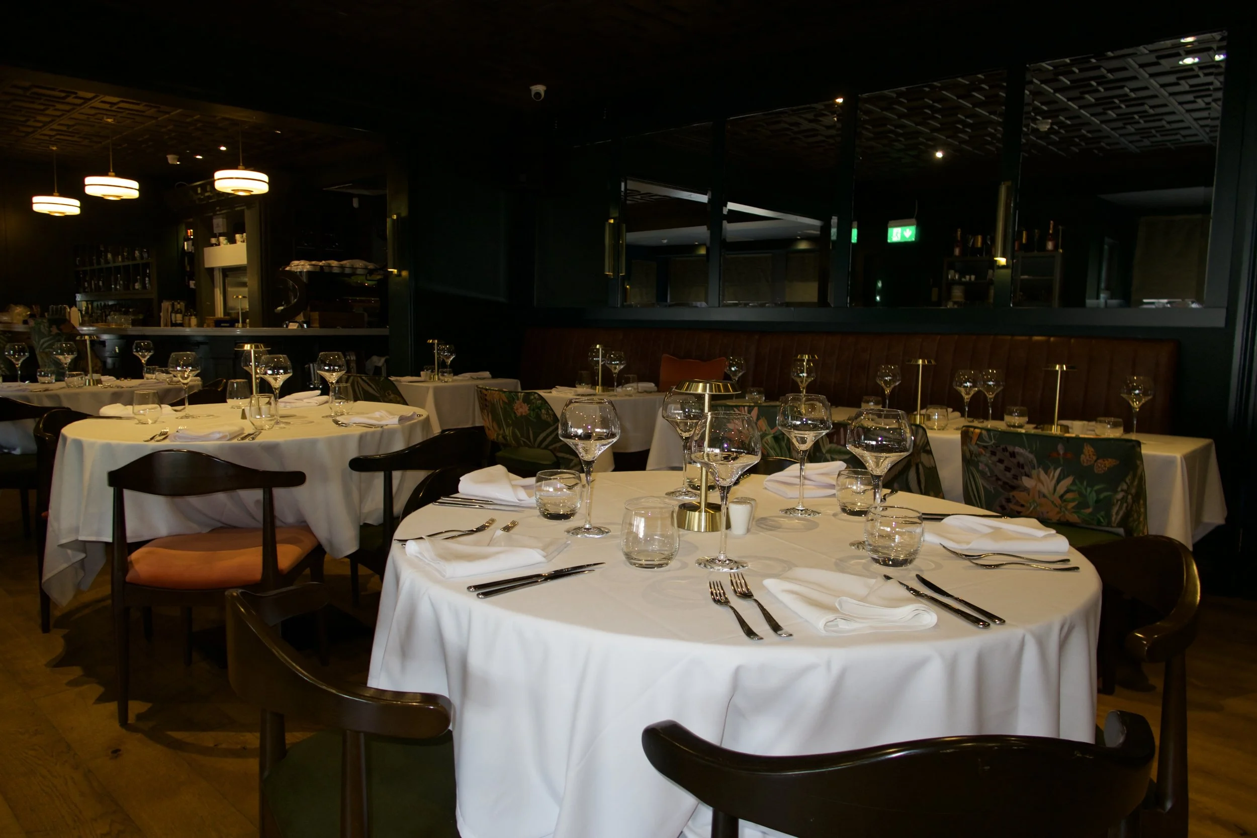 Elegant restaurant dining area with white tablecloths, glassware, and cutlery, dim ambient lighting, and a dark interior design.
