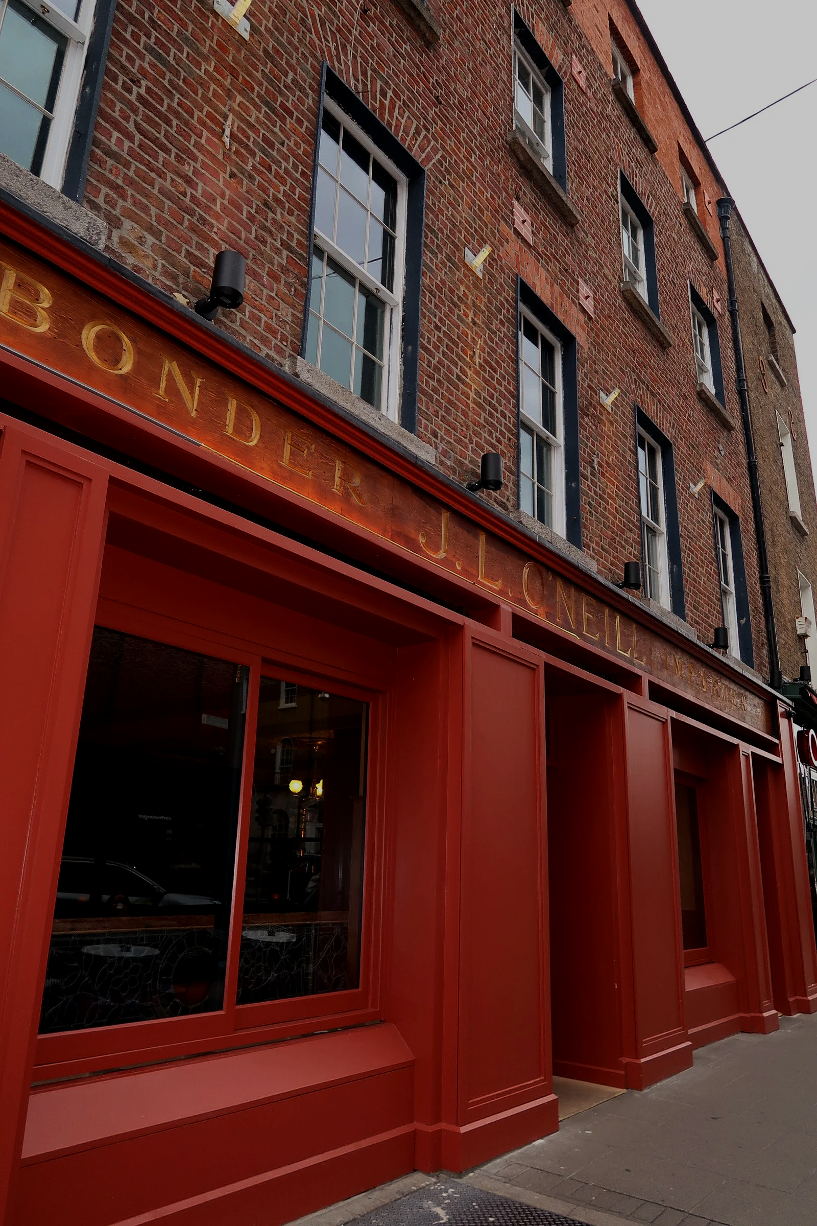 Red storefront with gold lettering above the door, large windows, and a brick building facade. Street scene with sidewalk and building details.