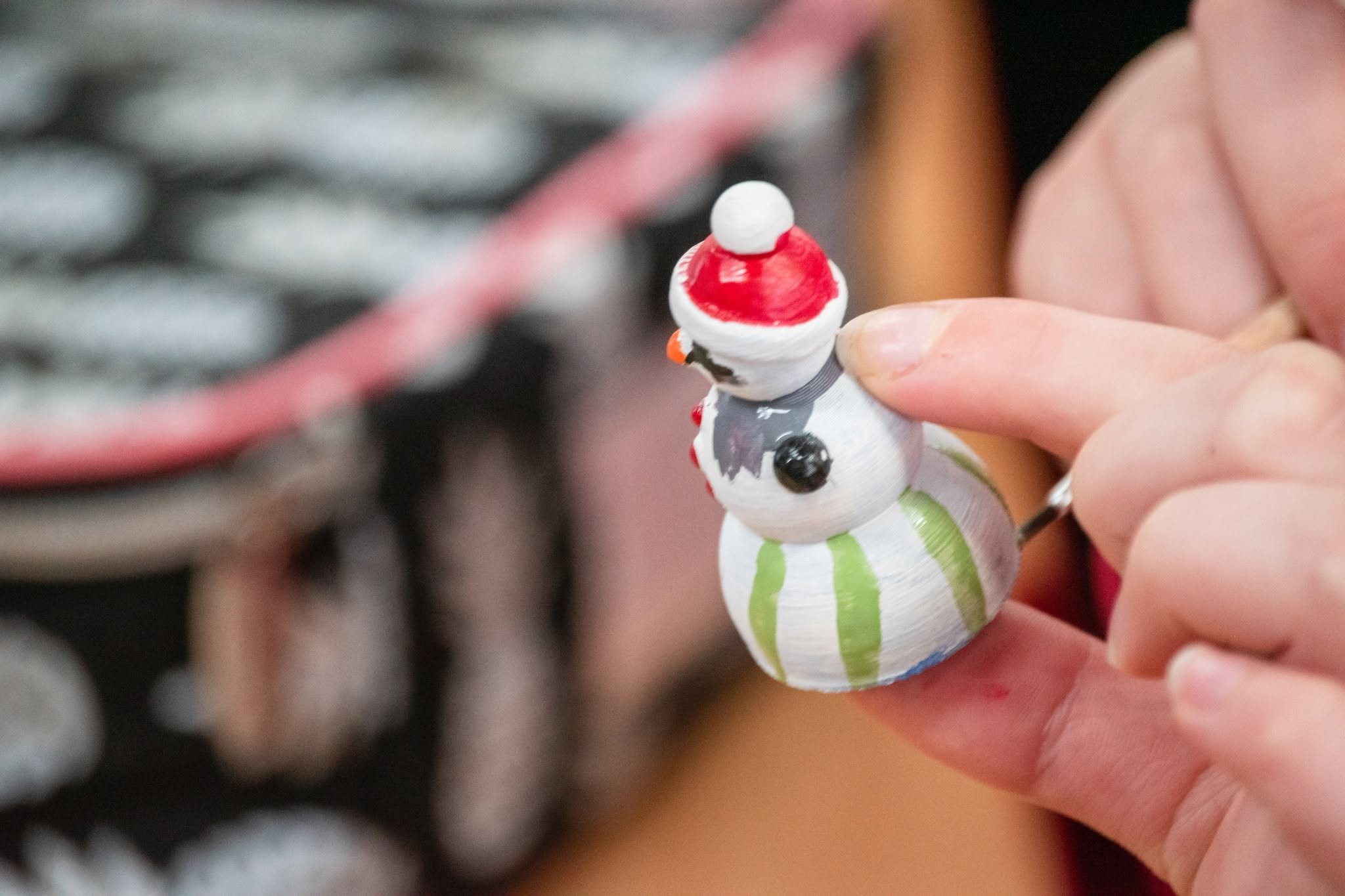 A person is holding a small, painted figurine of a snowman wearing a red hat and green scarf.