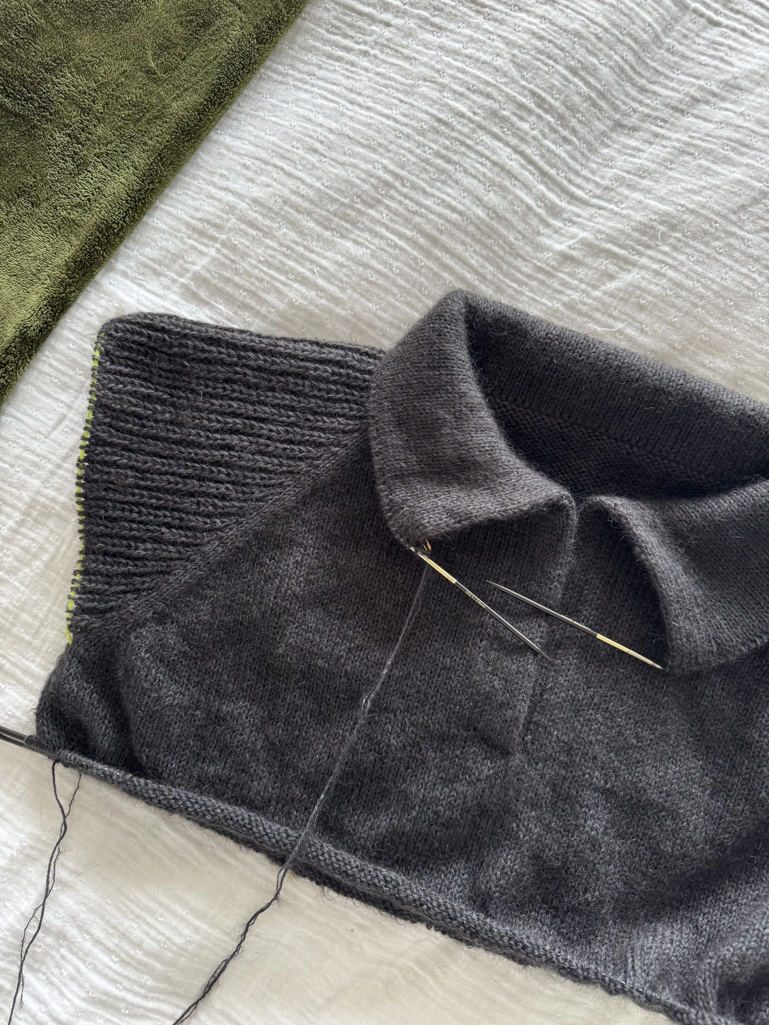 The First Polo, a knitting pattern by Hive Knits. Close-up of a dark inky blue-black knitted sweater work in progress with a polo collar, on a light-colored textured surface.