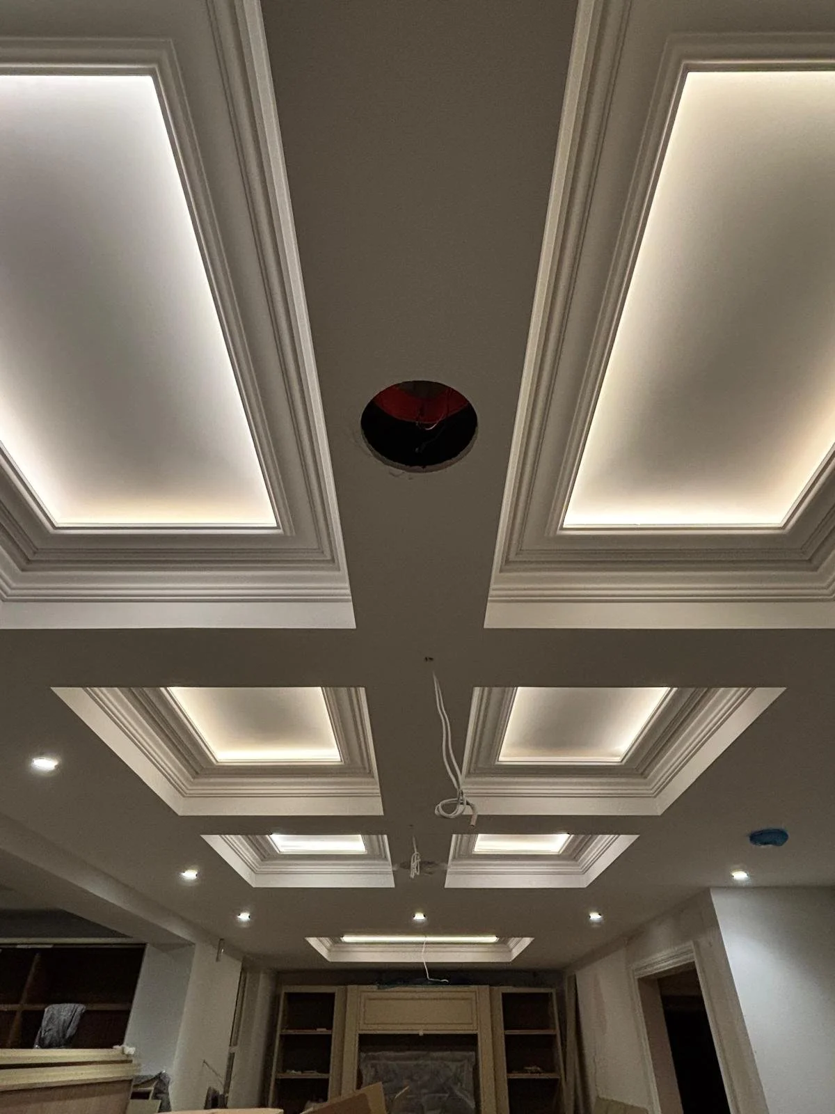 Ceiling with recessed lighting and decorative molding, a circular hole in the center with wires hanging, indicating ongoing installation or renovation.
