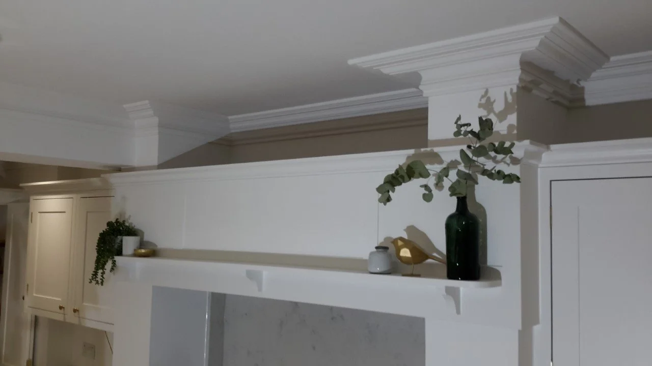 Interior view of a white built-in shelf with decorative items, including a green vase with eucalyptus, a small gray container, a golden bird figurine, and a small pot with trailing greenery, in a room with crown molding and white cabinetry.