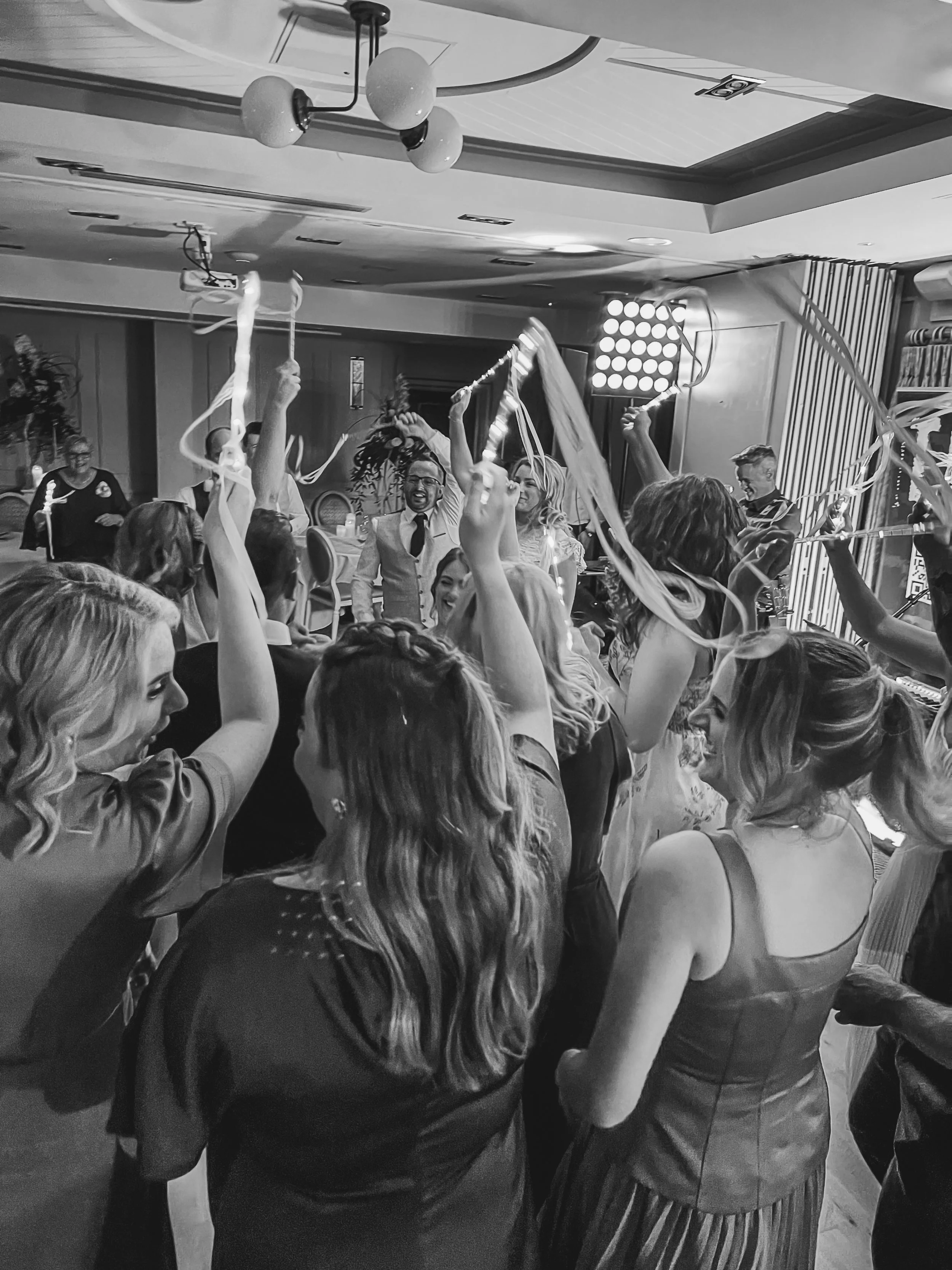 People celebrating at a party, dancing and waving streamers, with smiling faces, in a decorated room.