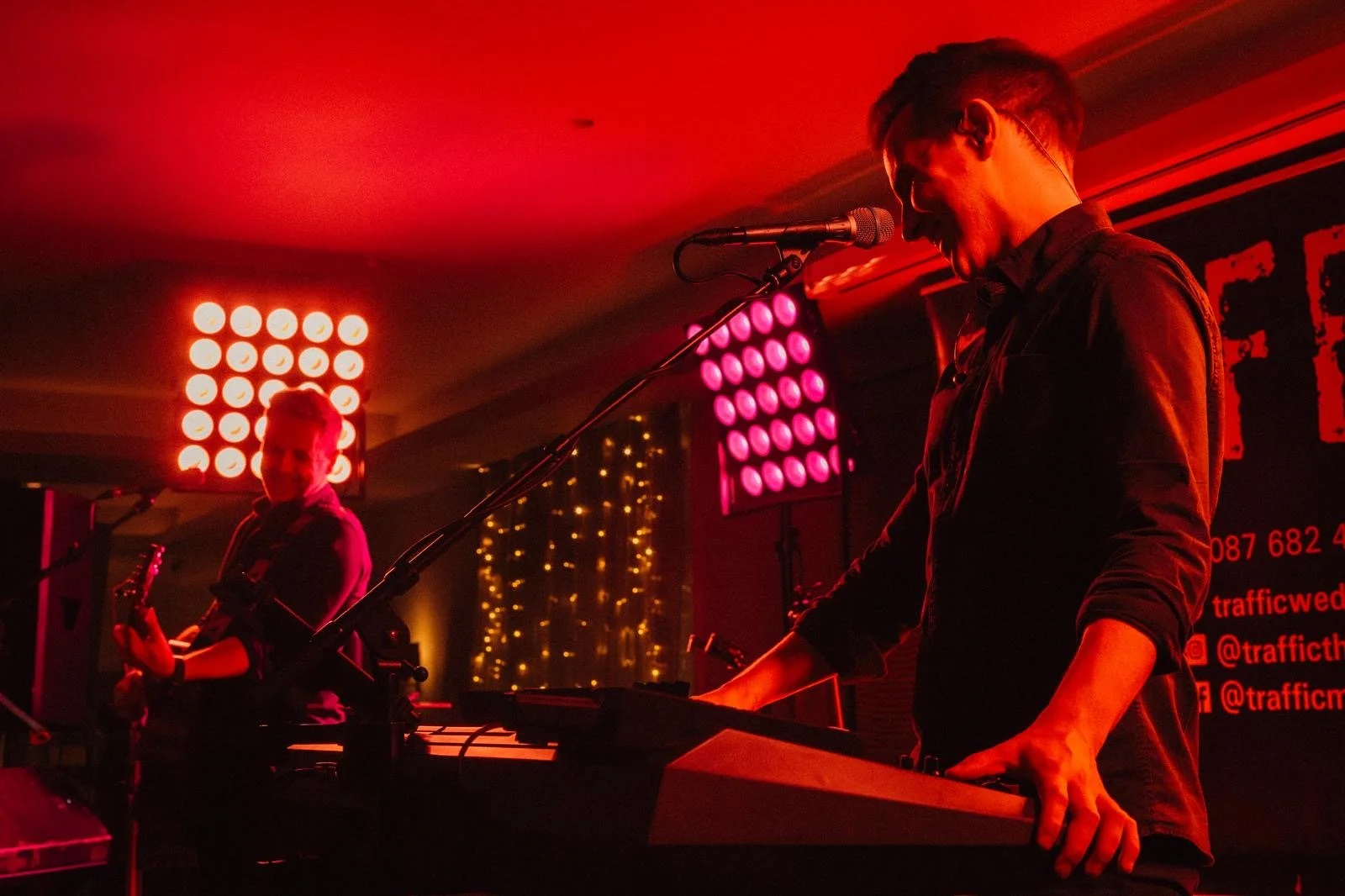 Traffic Wedding Band performing on stage with red and pink lighting, one playing guitar and the other playing keyboard, at a wedding reception.