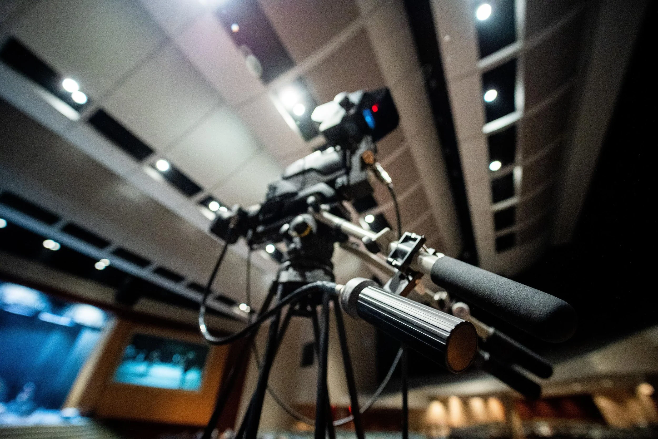 Close-up of a robotic arm or mechanical device with visible joints and wires, set against a background of ceiling lights and ceiling panels.