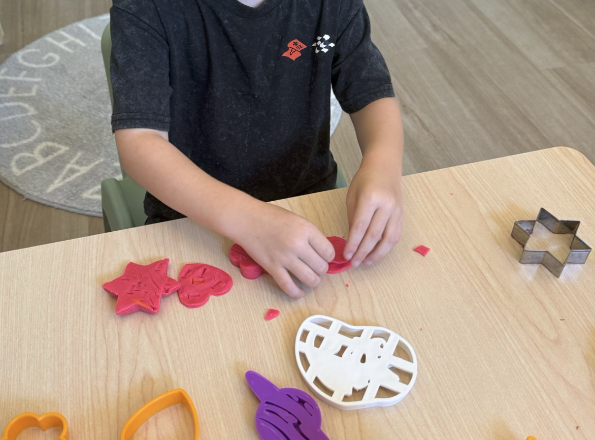 A child sitting at a wooden table playing with Play-Doh using cookie cutters.