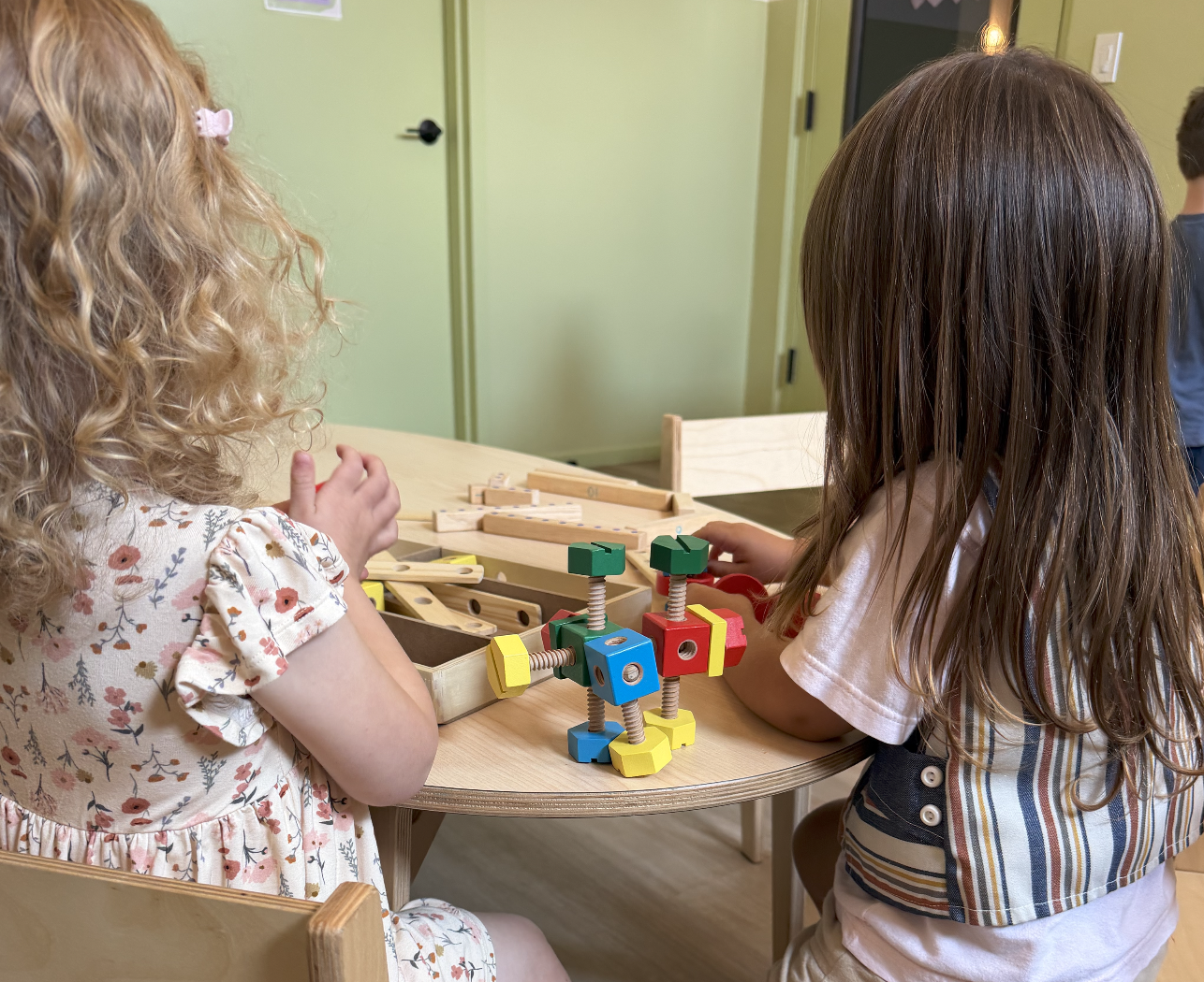 Two young girls playing with colorful wooden building blocks at a table.