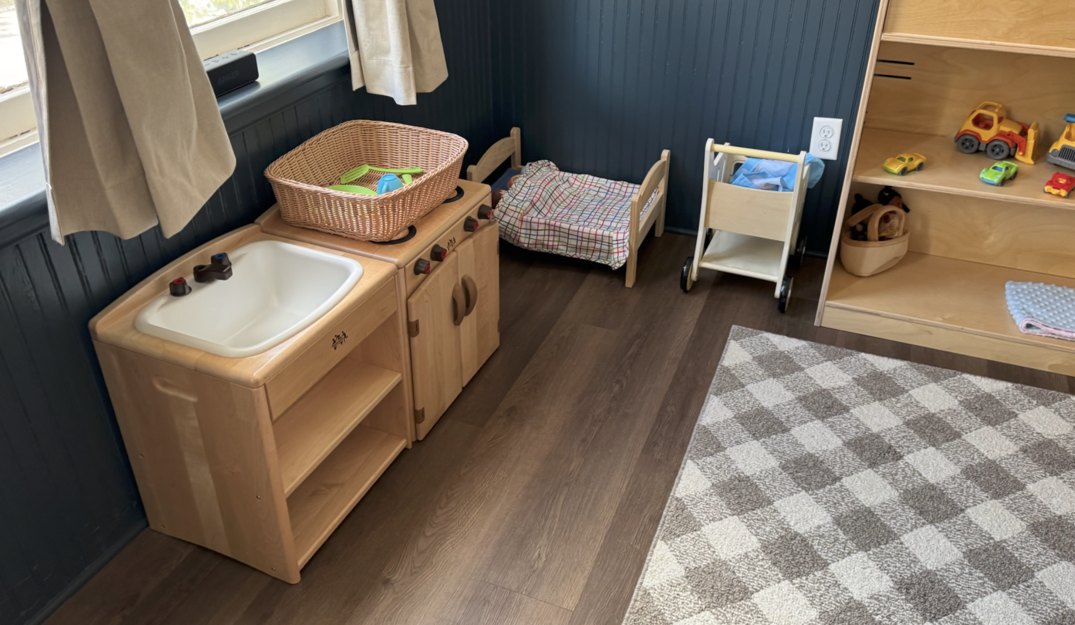 Children's playroom corner with toy sink, small wooden bed, toy trucks, and toy cars on shelves.