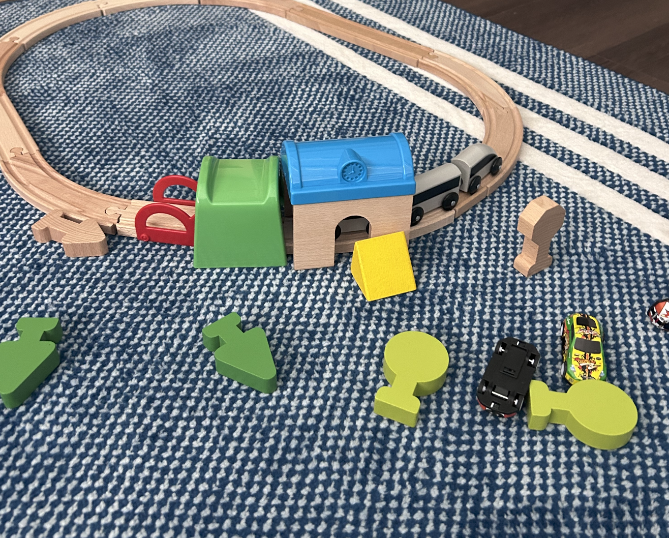 Montessori Children's wooden train set on a striped rug, with train cars, tracks, and colorful puzzle pieces.