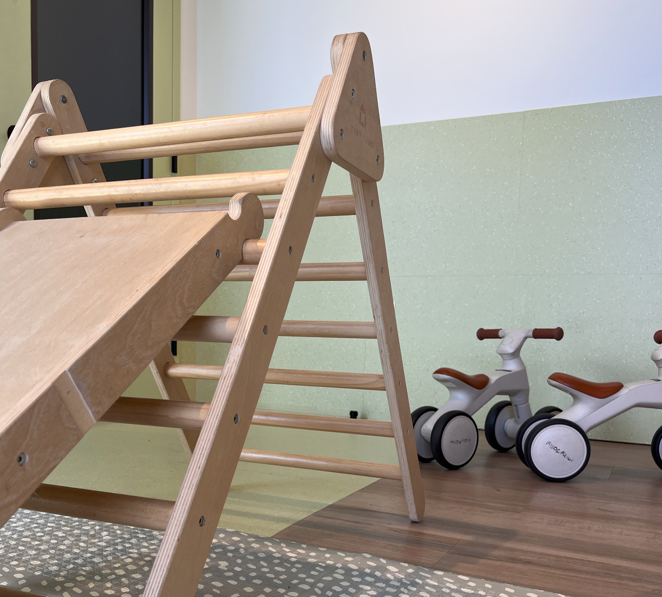 Indoor play area with a wooden slide and two white toy balance bikes.
