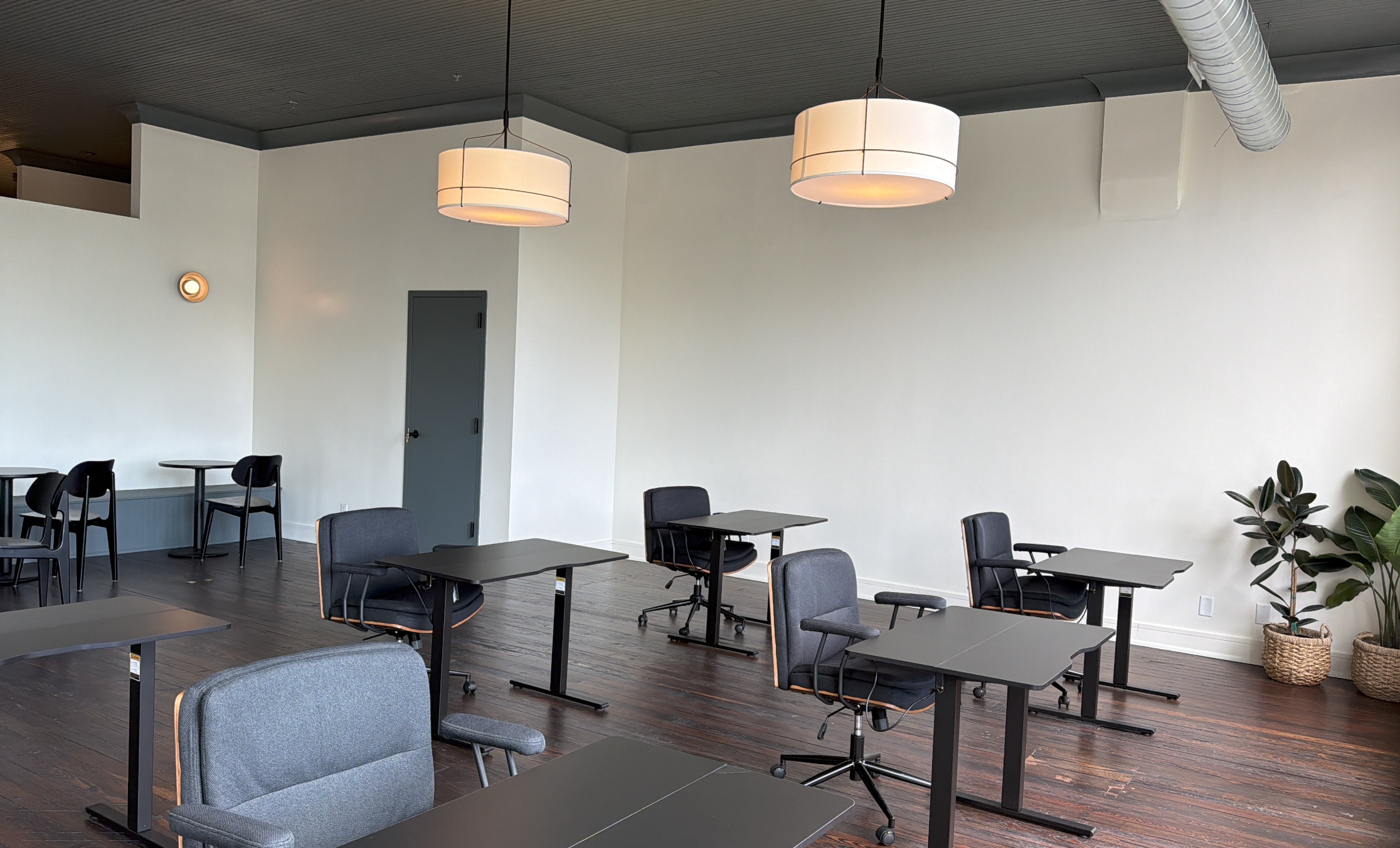 Interior of a modern coworking space with multiple tables and chairs, hanging ceiling lights, and plants.