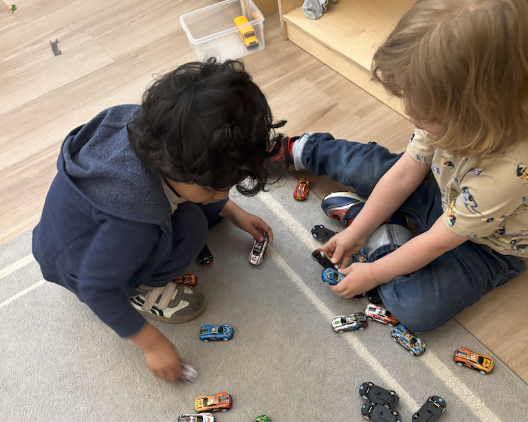 Two young children happily playing with toy cars on a gray rug.