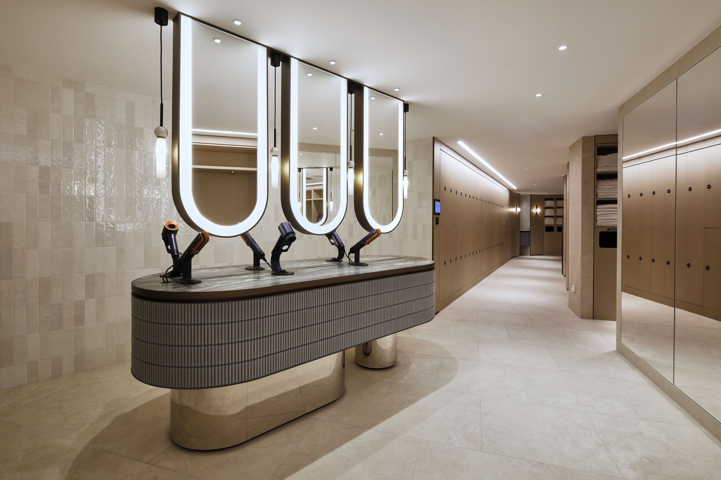 Modern hotel lobby with a circular check-in desk, large illuminated U-shaped sign, and beige tiled walls and floors.