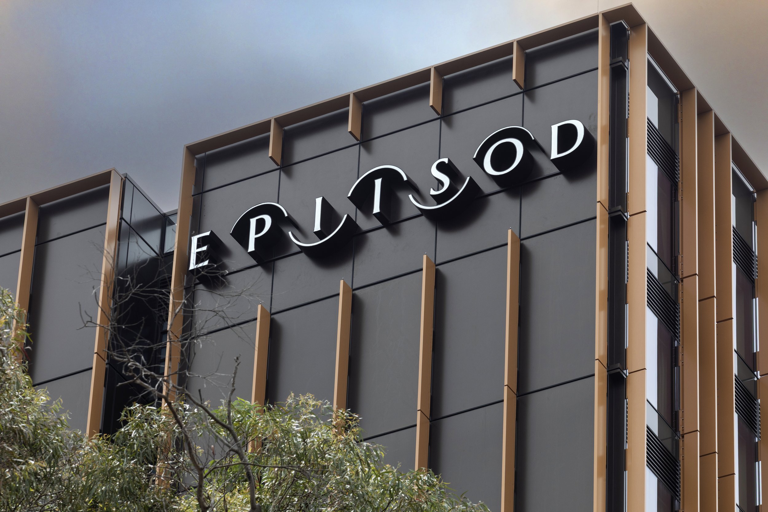 Modern building with black panelling and brown vertical batterns with a sign reading 'EPIISOD' on its facade.
