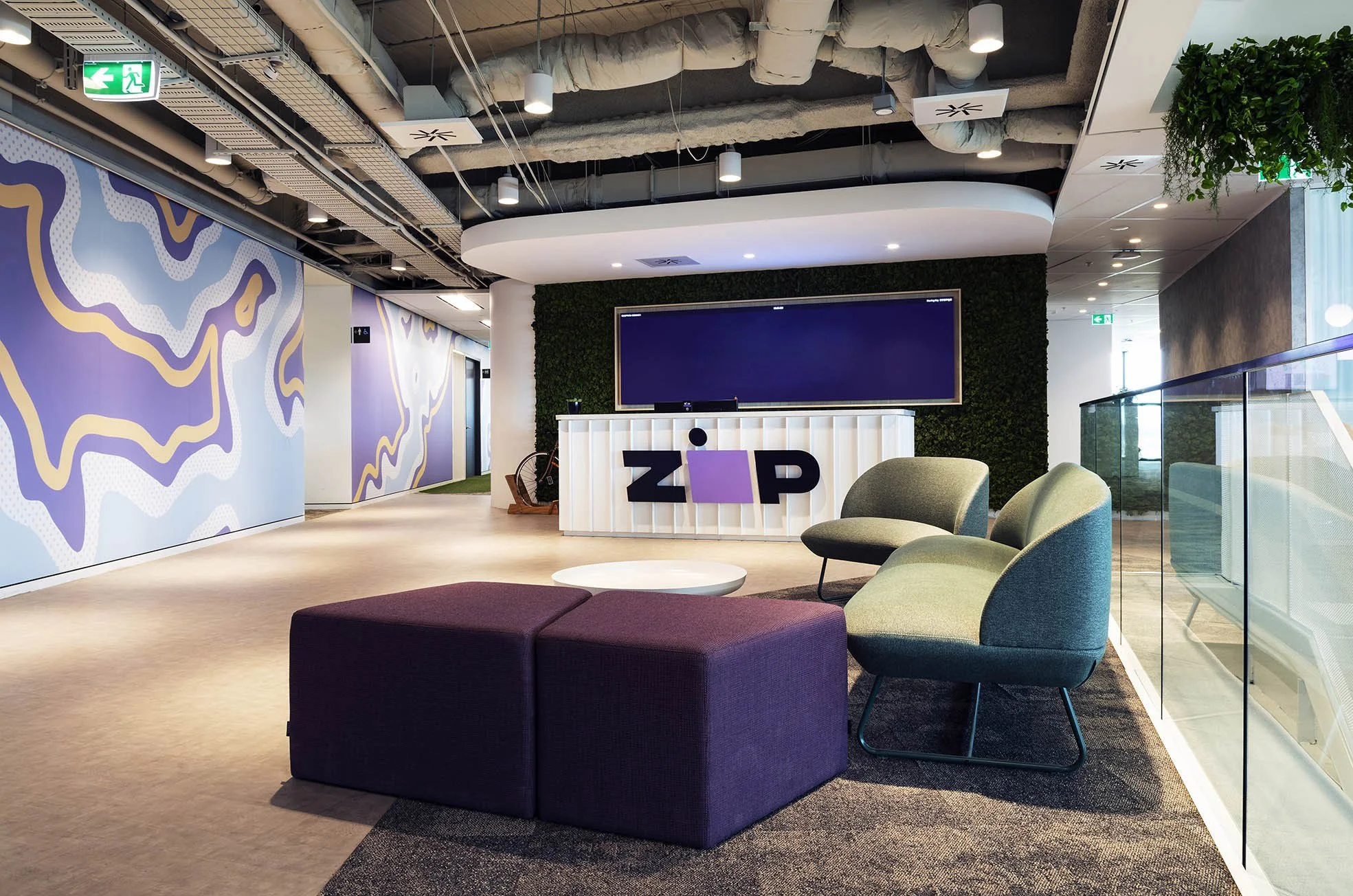 Modern reception lounge with purple and green seating, ZIP branding, decorative wall graphics, glass balustrade and an exposed industrial-style ceiling.