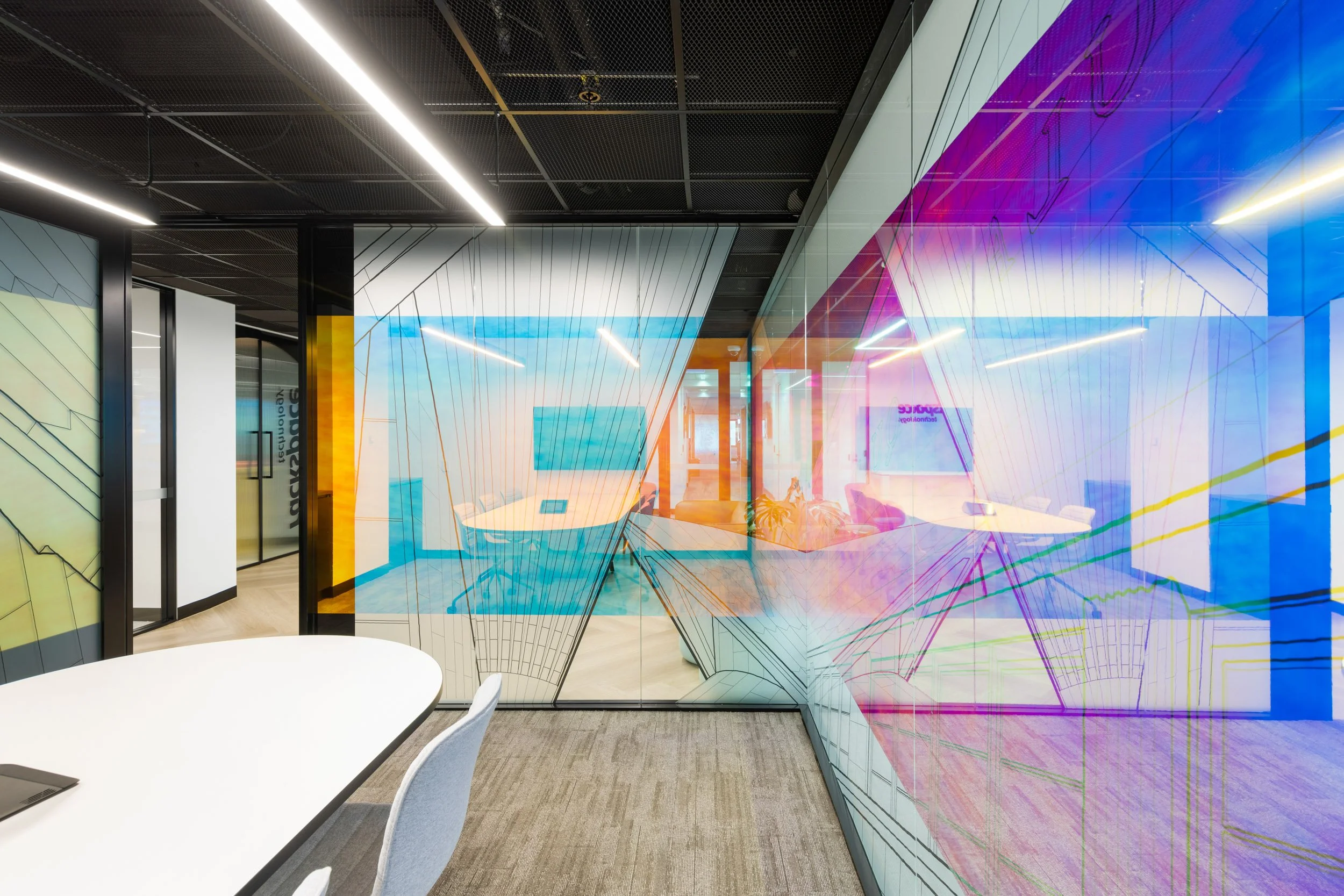 Modern conference room with a white round table and gray chairs, glass wall with colorful digital art, and ceiling with linear LED lighting.
