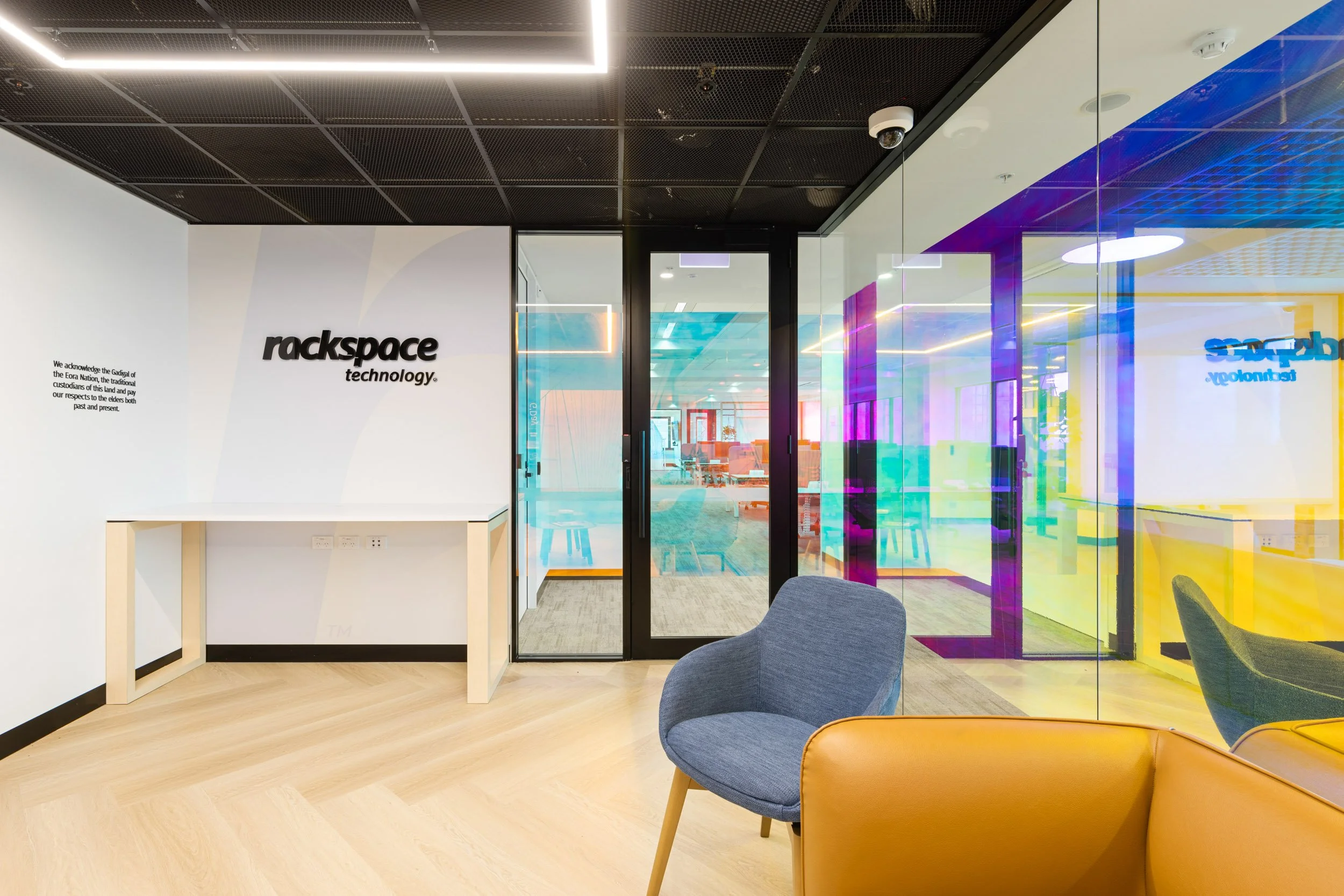 Modern office waiting area with glass walls featuring colourful dichroic film and Rackspace Technology signage.