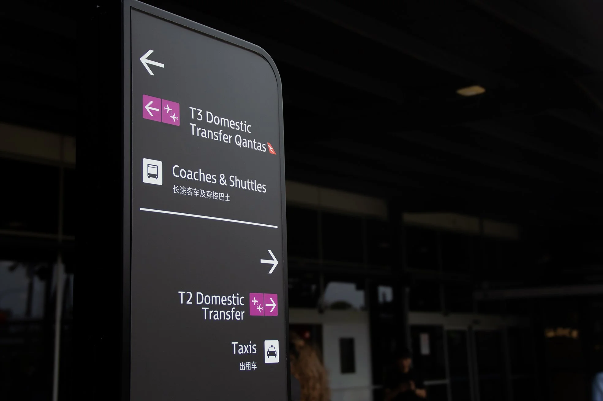 Airport sign showing directions for domestic transfer to Qantas, coach and shuttle services, and taxis.