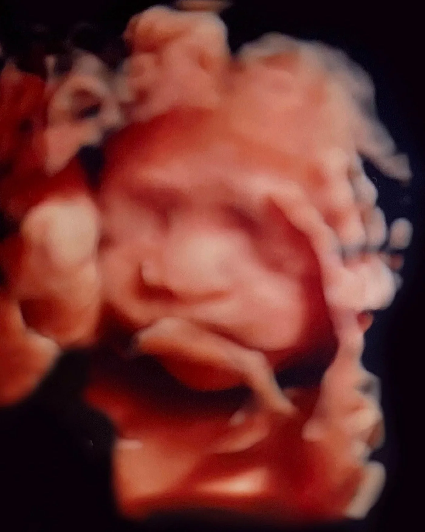 Close-up of a person's hand holding a small piece of food, possibly a pinkish meat or seafood, against a dark background.