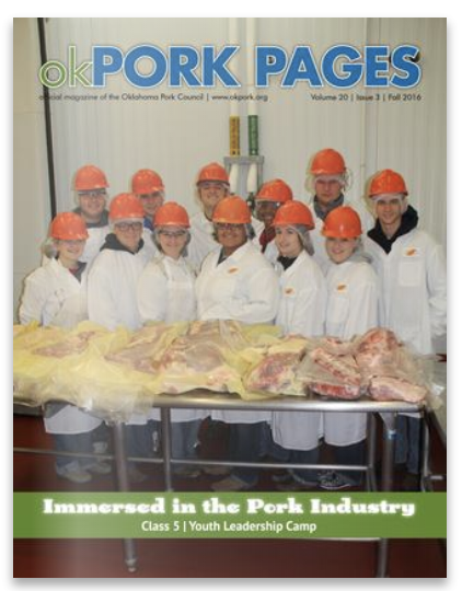 Cover of Oklahoma Pork Pages featuring a group of people wearing white coats and orange safety helmets standing behind a table with large pieces of pork, in an industrial or processing facility.