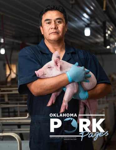 A man wearing a navy blue shirt and blue gloves holding a piglet in a pig farm or processing facility.