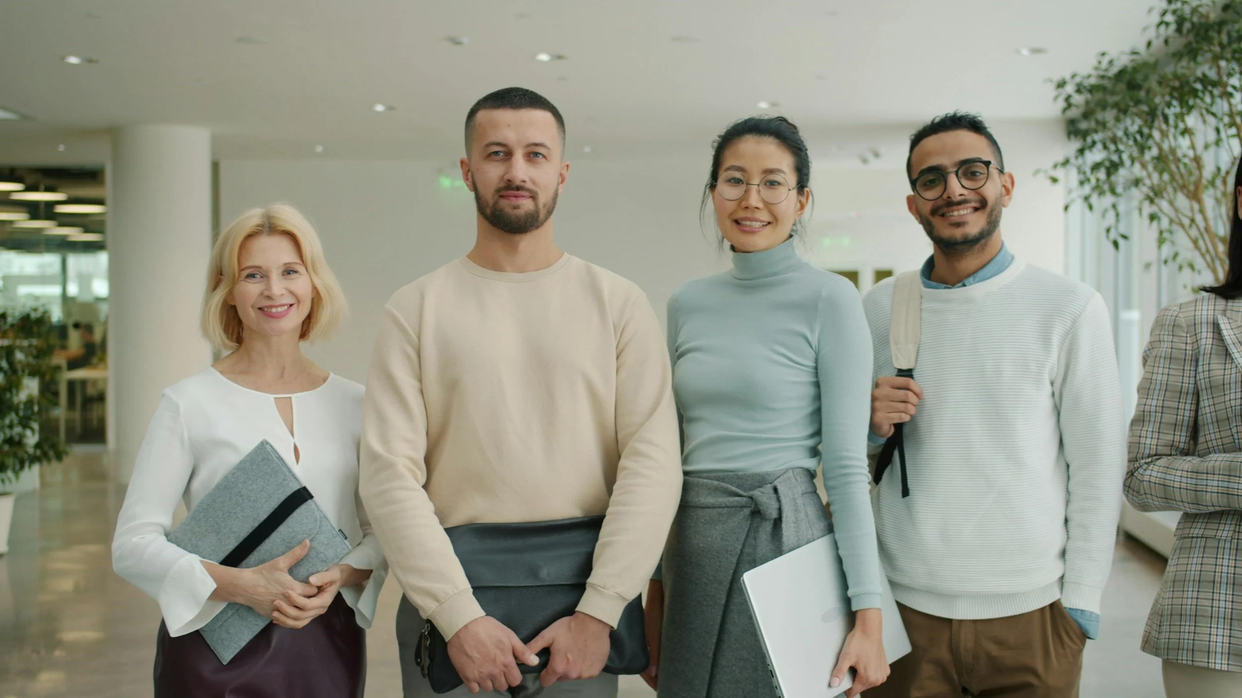 Group of diverse professionals in an office building lobby, smiling and holding folders or laptops.