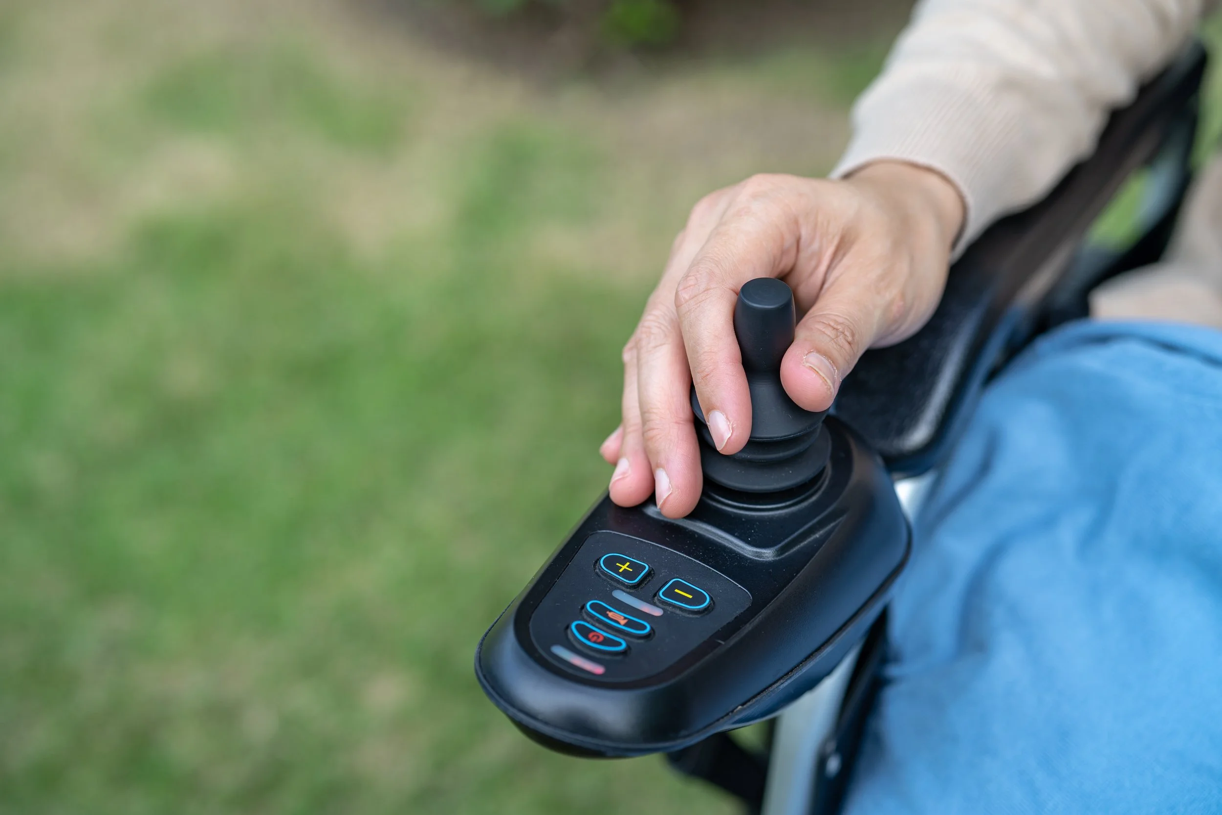 Person's hand on a joystick or controller mounted on a wheelchair.