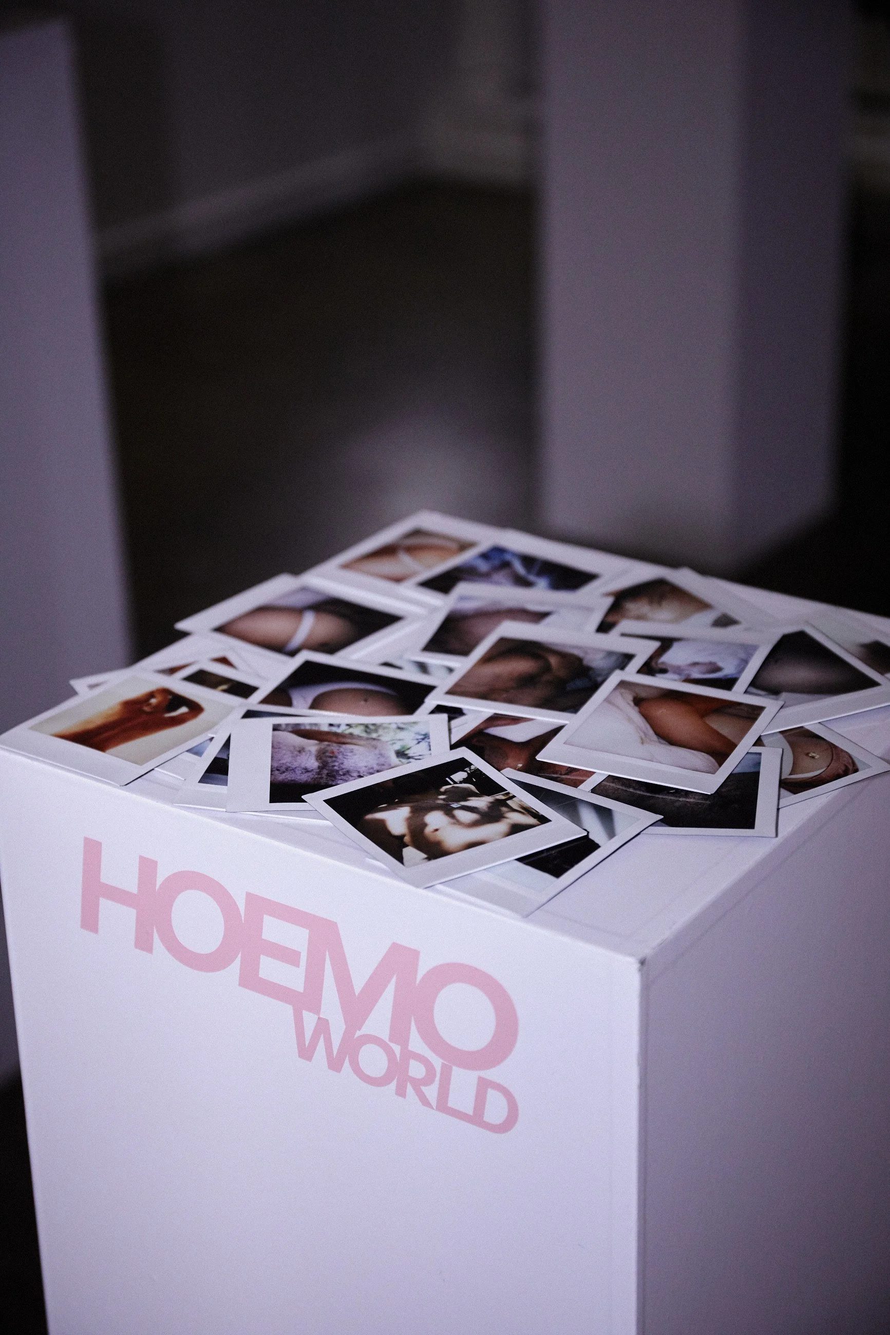 A white box with pink text that reads 'HOME' and 'WORLD' partially visible, with scattered printed photographs on top, showing various images including people and objects.