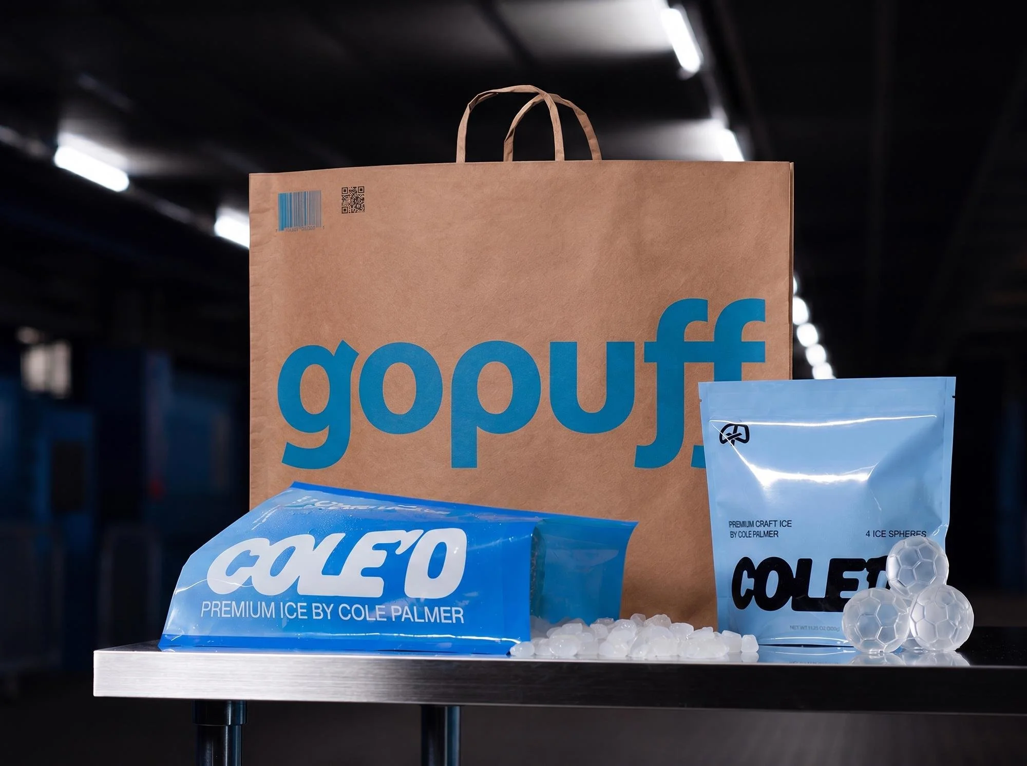 A paper shopping bag with blue 'gopro' branding in the background, and blue Cole Palmer ice packaging in the foreground with ice cubes, on a metal surface.