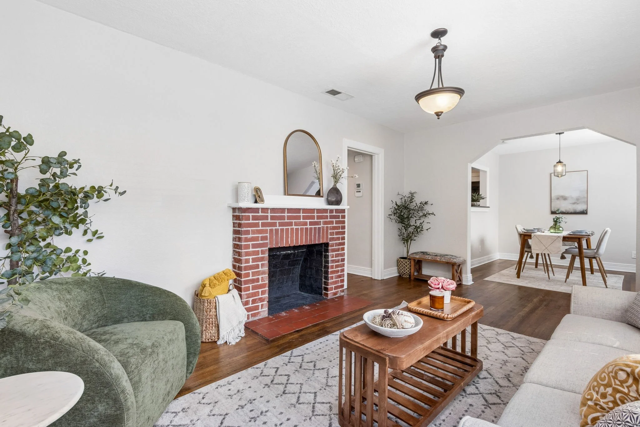 Living room with a brick fireplace, green sofa, white furniture, and wooden decor, decorated with plants and accessories.