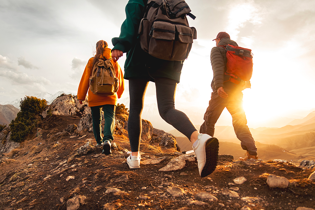 Trois randonneurs avec des sacs à dos marchant sur une crête montagneuse au coucher du soleil