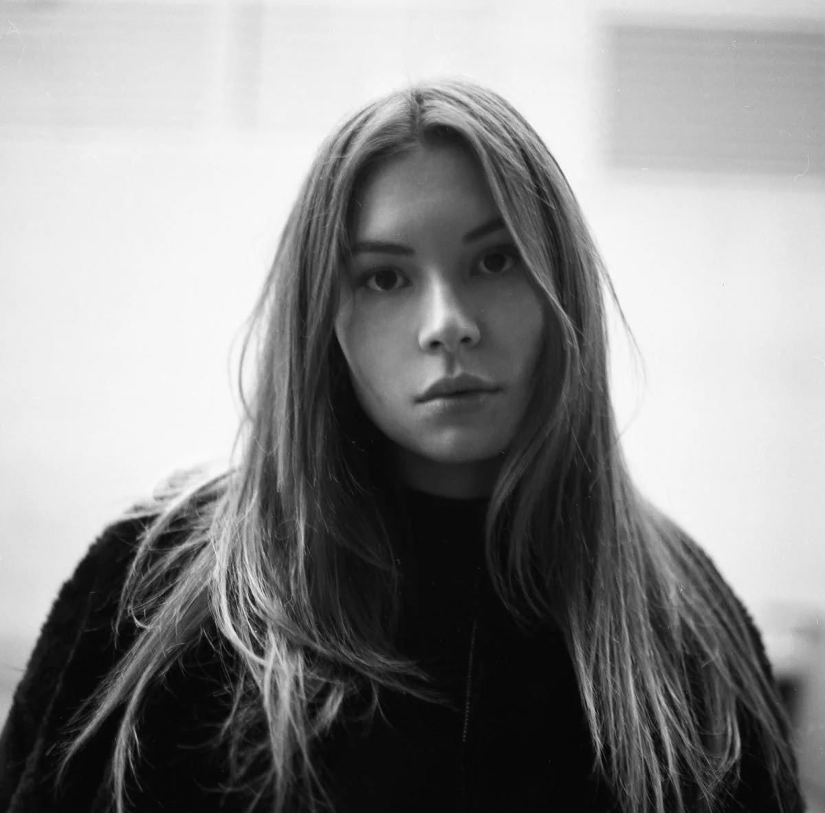 Portrait en noir et blanc d'une jeune femme avec cheveux longs, veste noire, regard fixe.