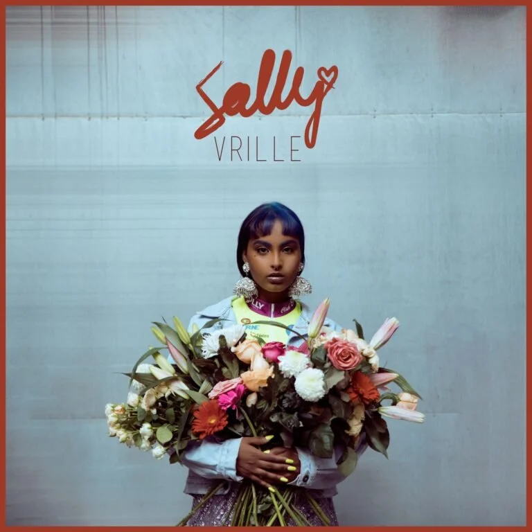 Une jeune femme noire porte de grosses boucles d'oreilles, un blazer blanc, et tient un grand bouquet de fleurs colorées devant un mur gris, avec un logo 'Sally VRILLE' en rouge au-dessus.